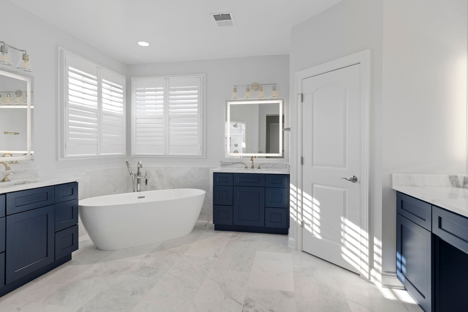 Custom bathroom vanity installation: deep blue shaker vanities, marble counters, and freestanding tub setup.