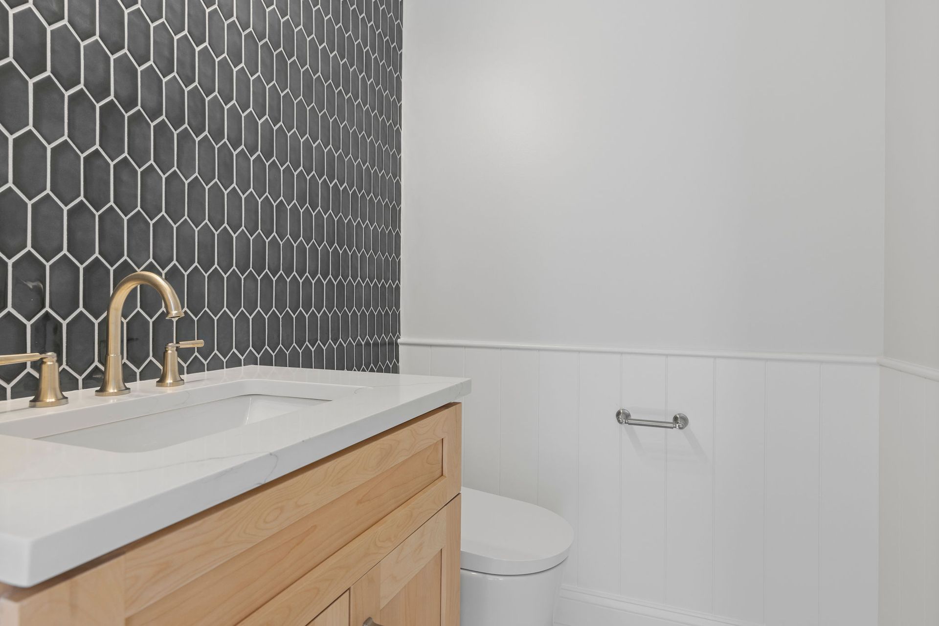 Powder room remodeling: installing dark hexagon tile accent wall, wood vanity, and gold fixture accents.