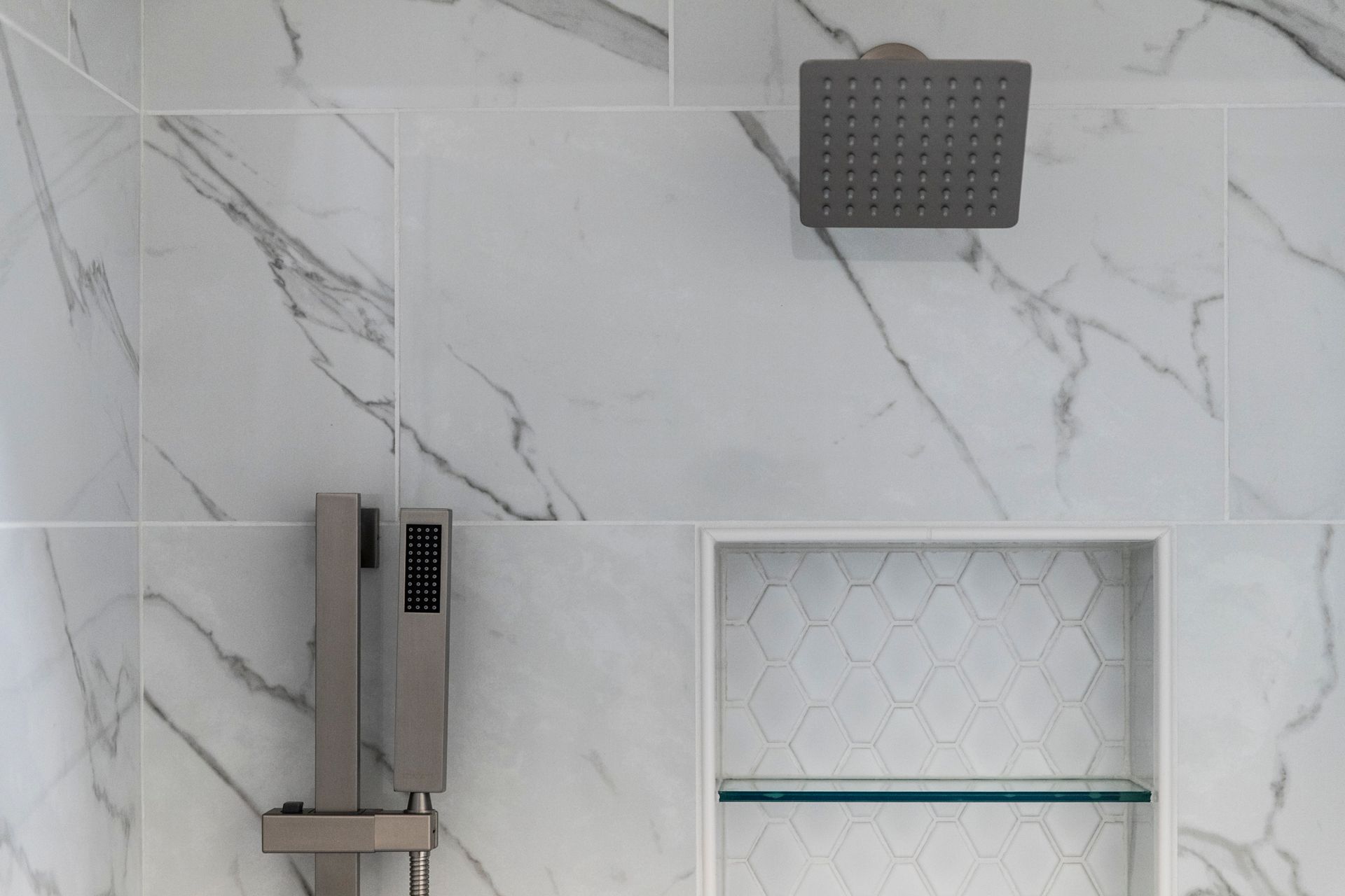 A shower niche with hexagonal tiles and a glass shelf.