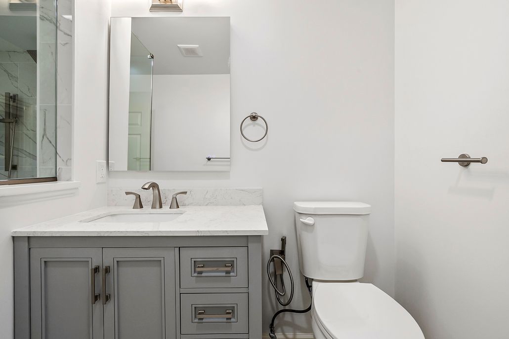 A modern bathroom with a gray vanity, toilet, and white walls.