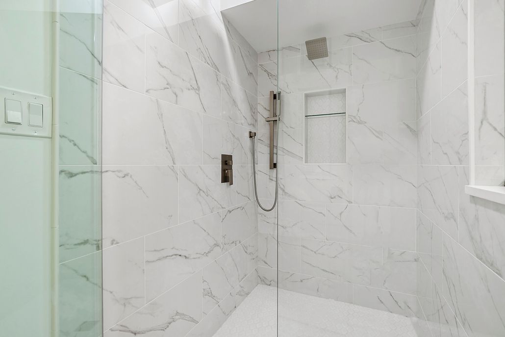 A walk-in shower with white marble-style wall tiles and hexagonal floor tiles.