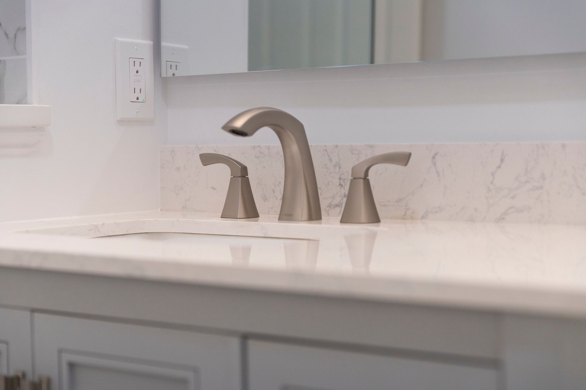 A close-up of a brushed metal faucet on a white marble-style countertop.
