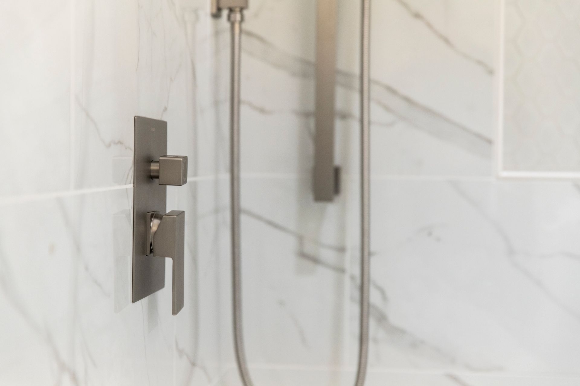 A close-up of a brushed metal shower control on a marble-style wall.