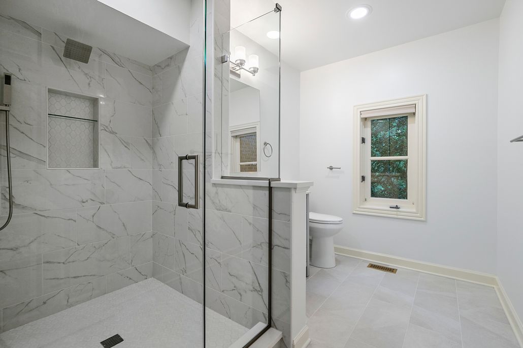 A modern bathroom with a white marble-style shower and light gray floors.