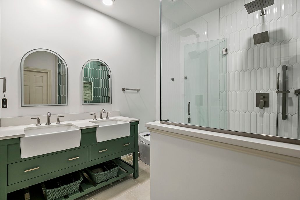 Custom bathroom design and build featuring contrasting green vanities, custom tile work, and luxurious walk-in showers for modern homes.