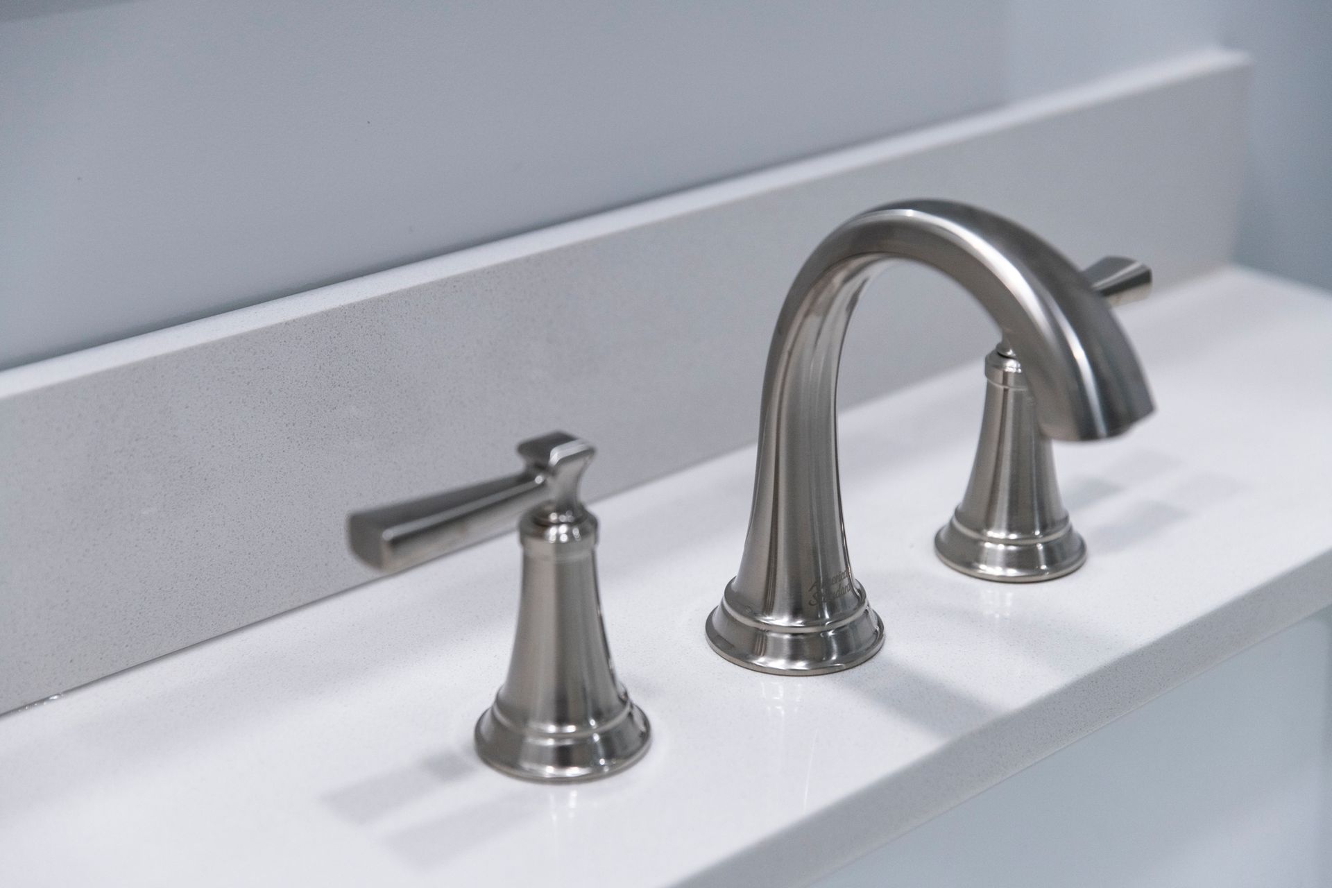 Precision installation of transitional brushed nickel plumbing fixtures on white quartz, emphasizing quality craftsmanship in every detail.