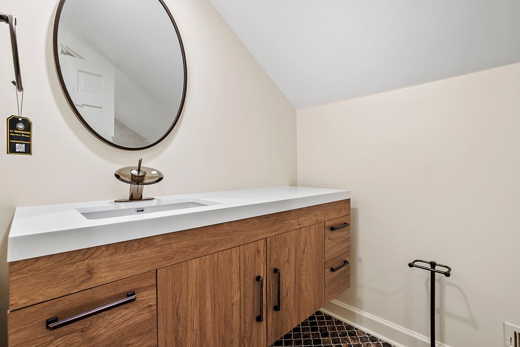 After photo of a modern Towson bathroom featuring a new dark wood floating vanity, white countertop, and a sleek black round mirror.