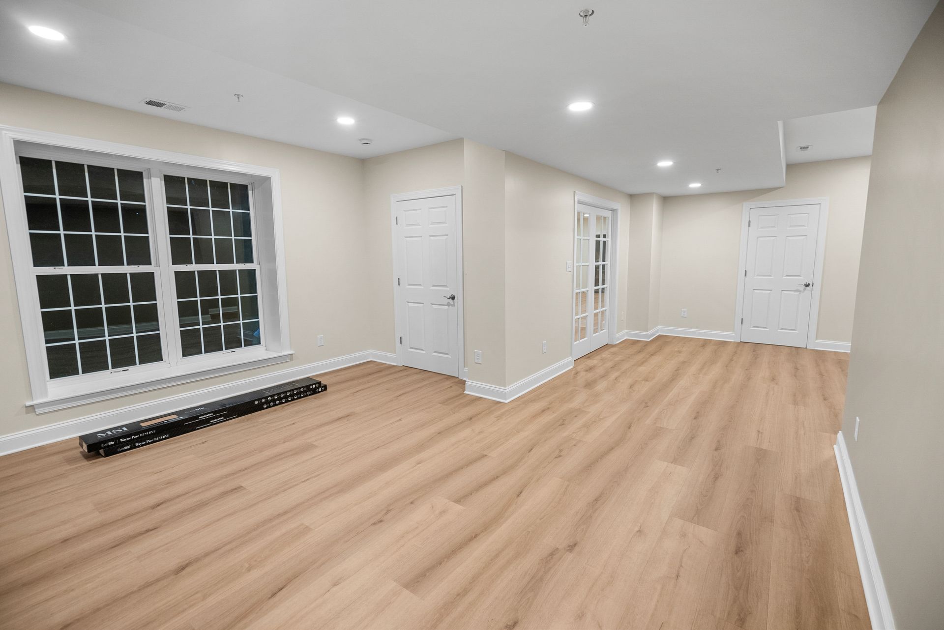 Wide-angle view of a finished basement space with warm LVP flooring, light tan walls, and recessed LED illumination.