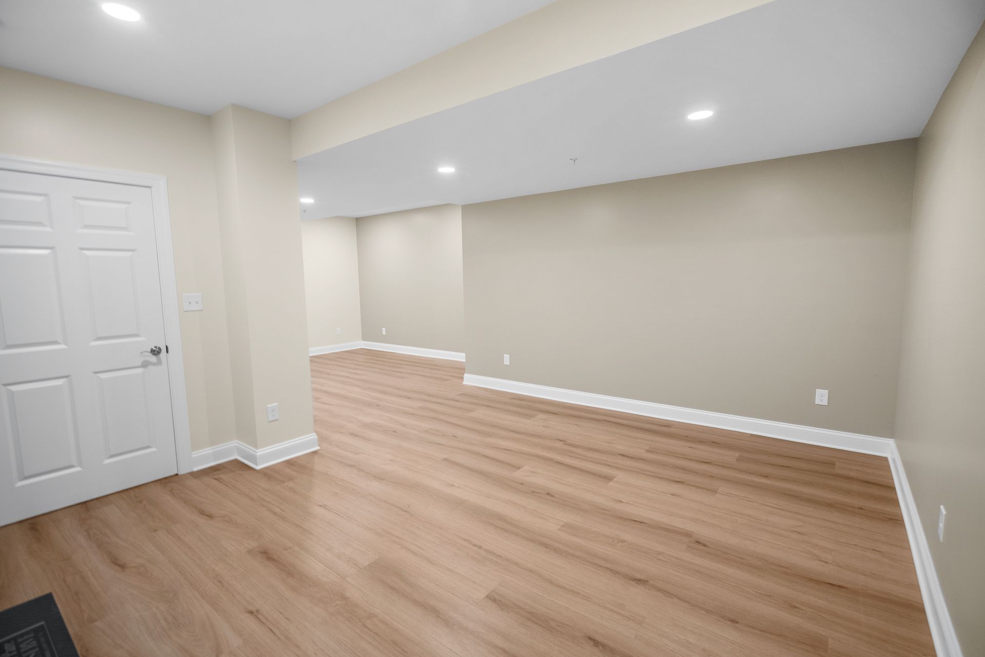 Open lower-level recreation room with continuous wood-look flooring and custom wall soffits.