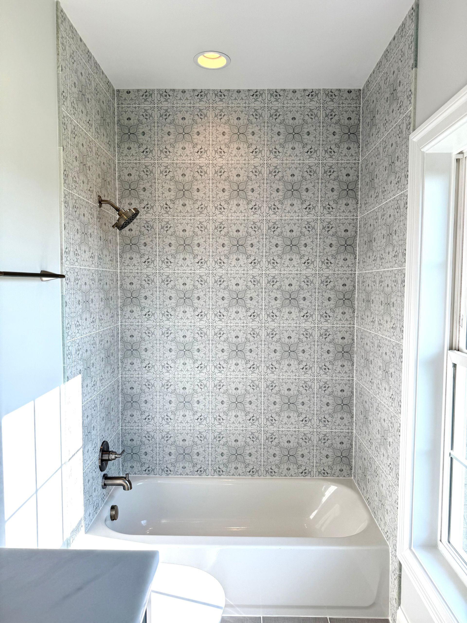 A view of the elegant new bathtub and nickel shower fixtures against the patterned tile wall.