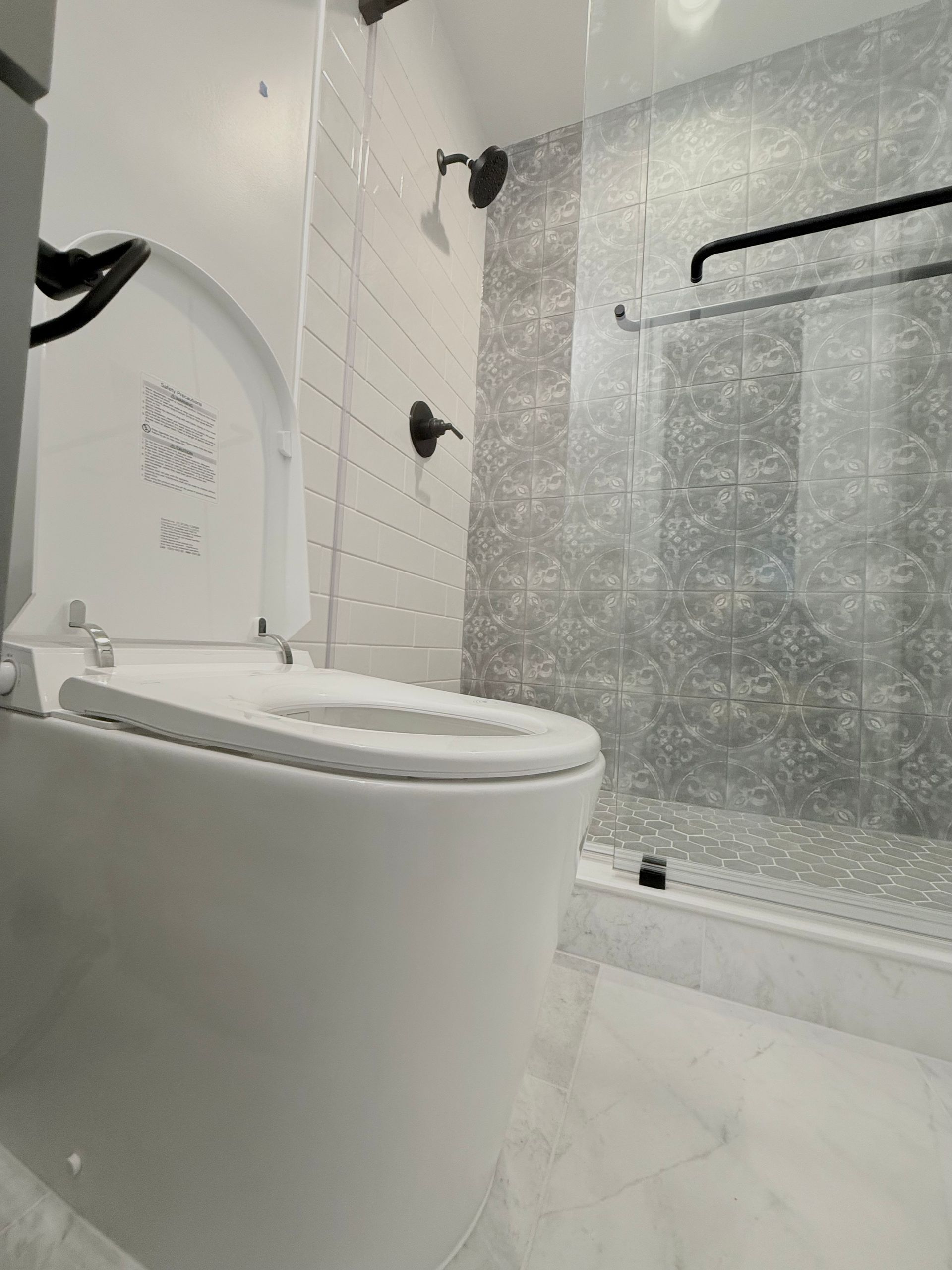 A new white toilet and modern shower conversion with patterned wall tiles in a Hampstead home.