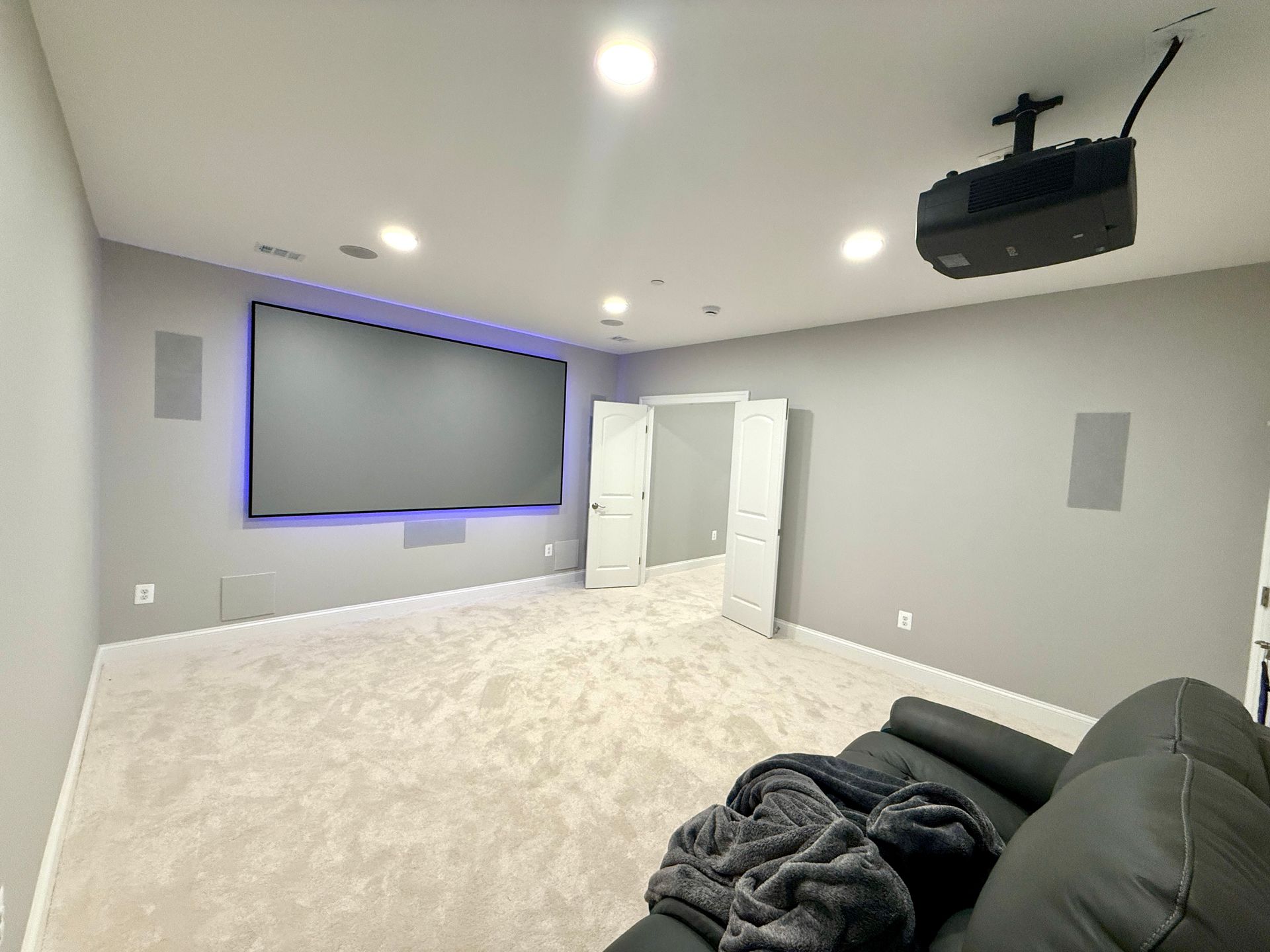 A home theater with ambient lighting behind the screen, plush carpeting, and a comfortable leather sofa.
