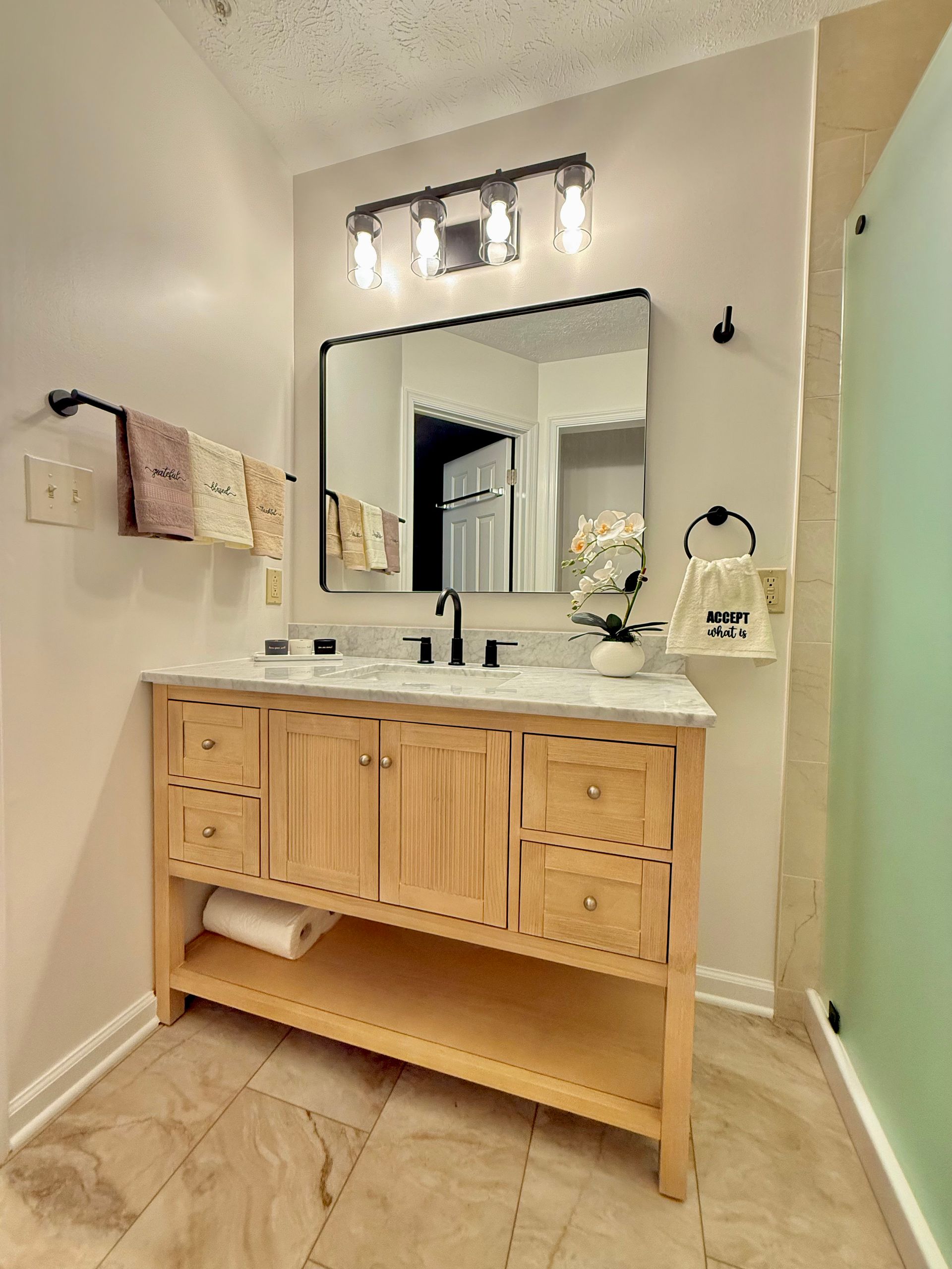 Modern bathroom renovation featuring purchased wood vanity, black hardware, and expert tile work.