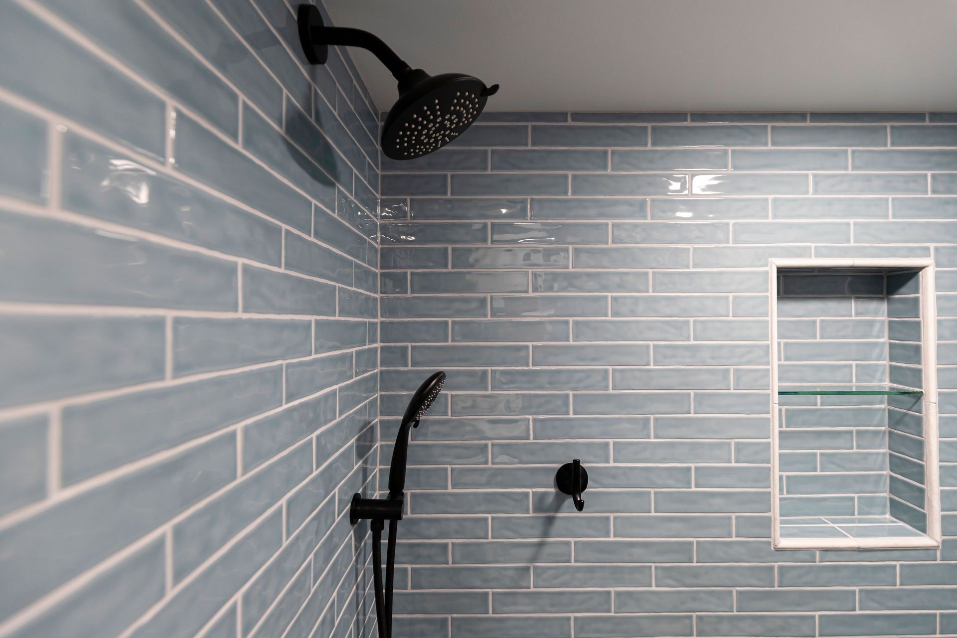 Close-up of the tiled shower niche, glass shelf, and matte black fixtures in a tub-to-shower conversion.