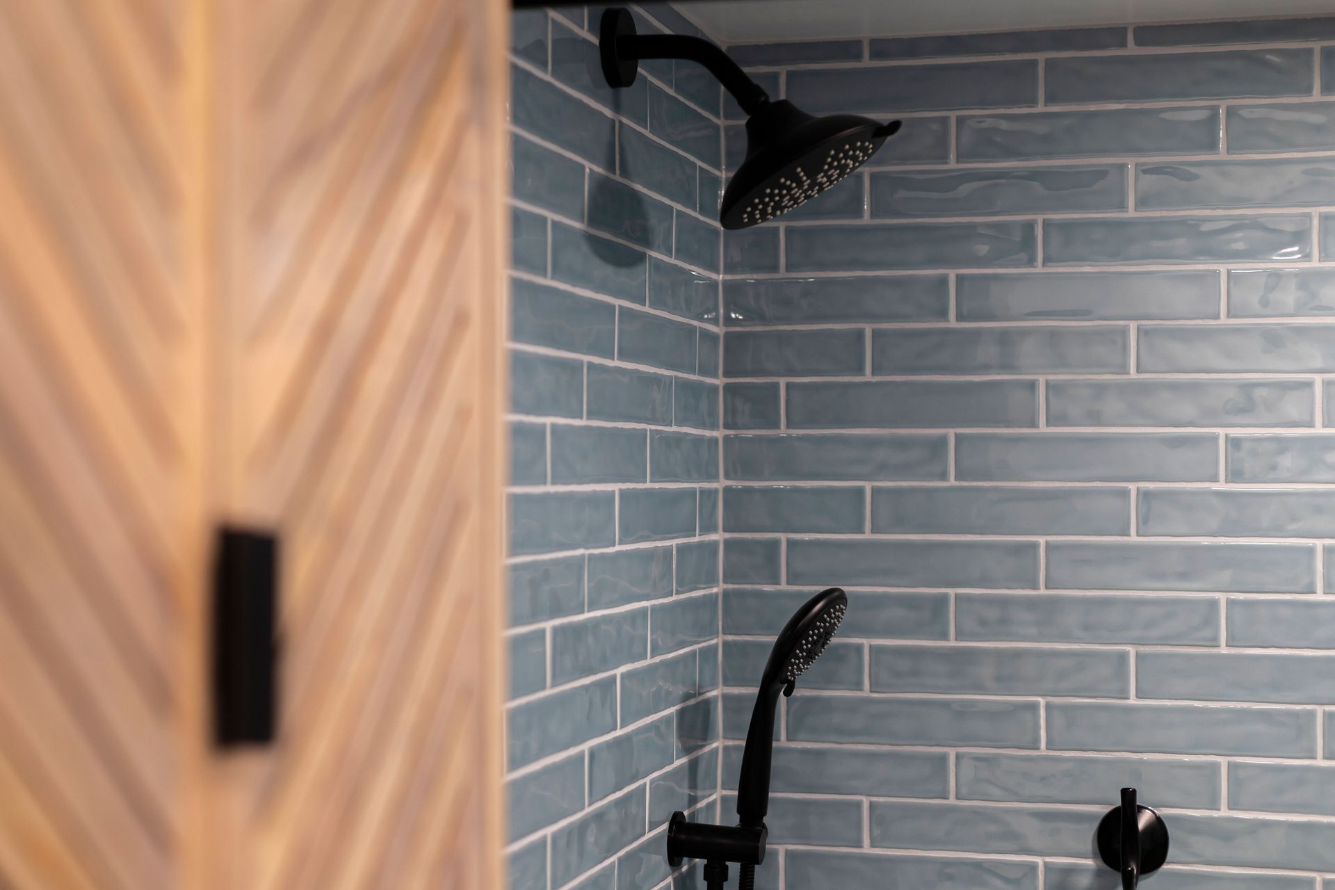 Close view of the matte black fixtures (rain shower/handheld) against the blue tile, showing the custom wall cabinet edge.
