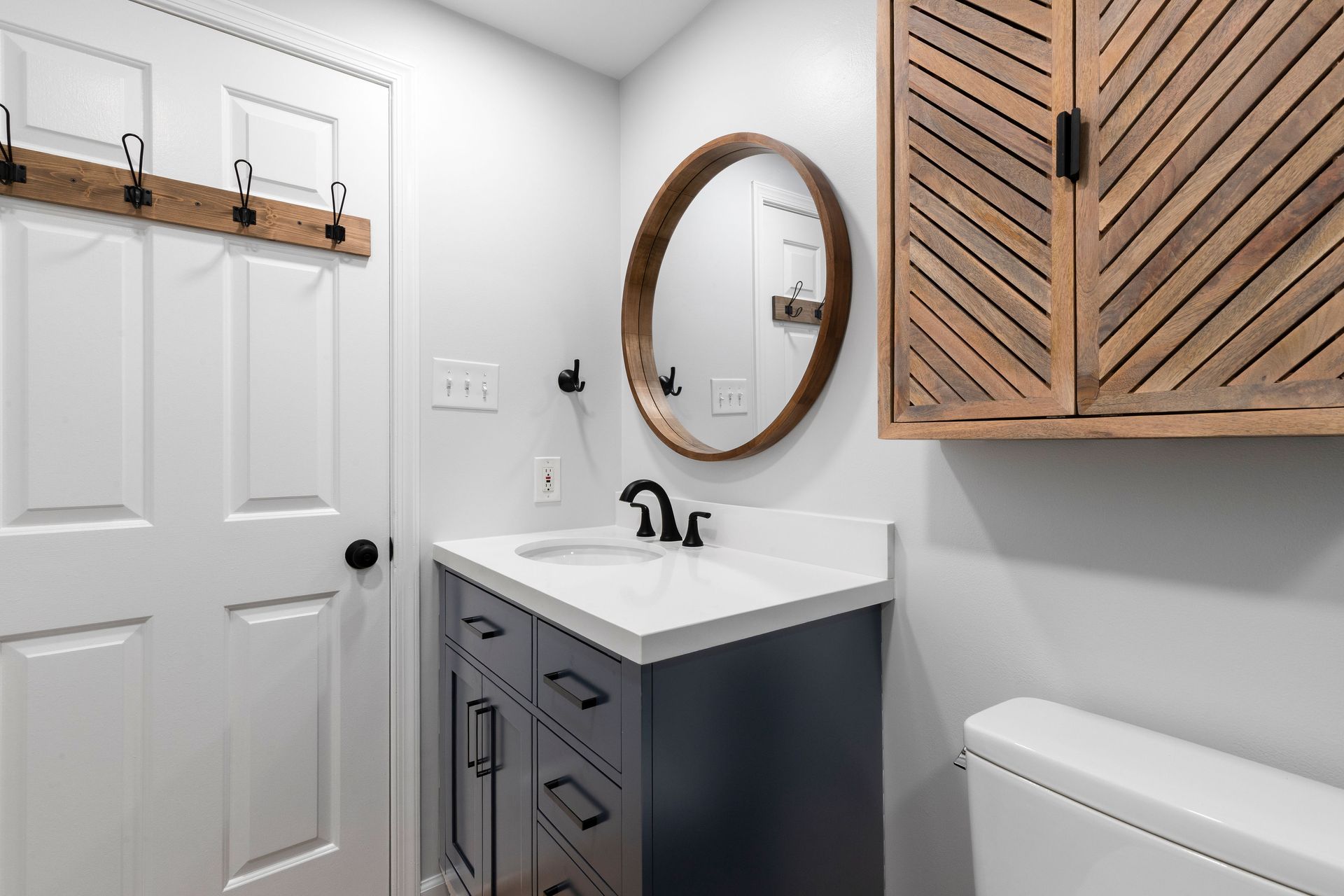 Wide view of the black vanity and custom wood wall cabinet near the entry door in the Ellicott City bathroom.