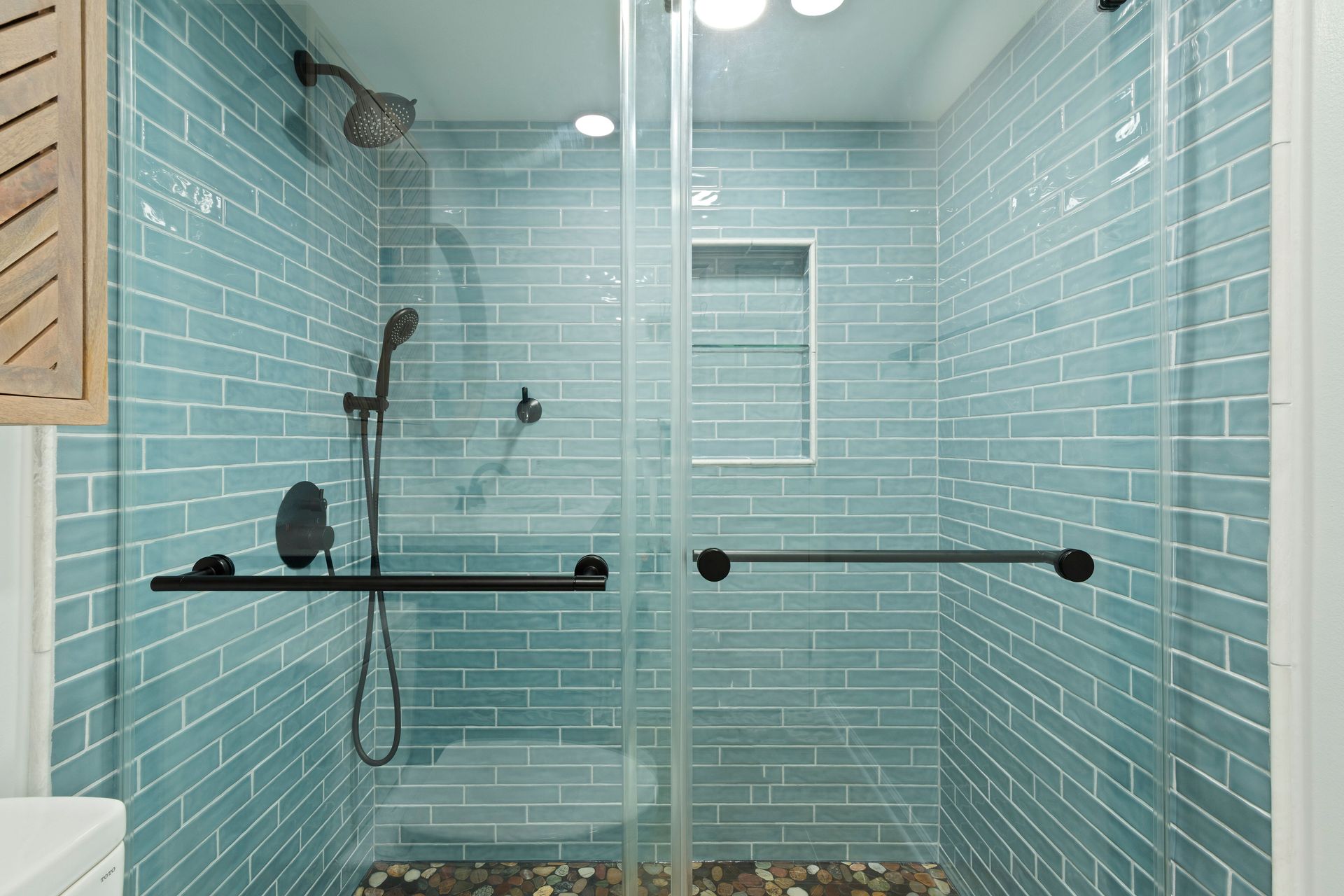 Full view of the frameless glass enclosure and blue subway tile walls over the pebble floor in the walk-in shower.