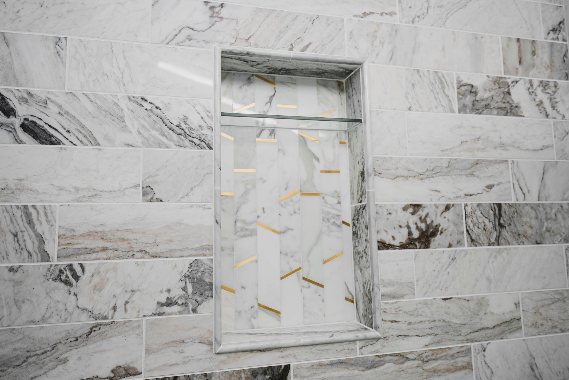 Close-up of a custom recessed shower niche with geometric mosaic tile and gold accents.