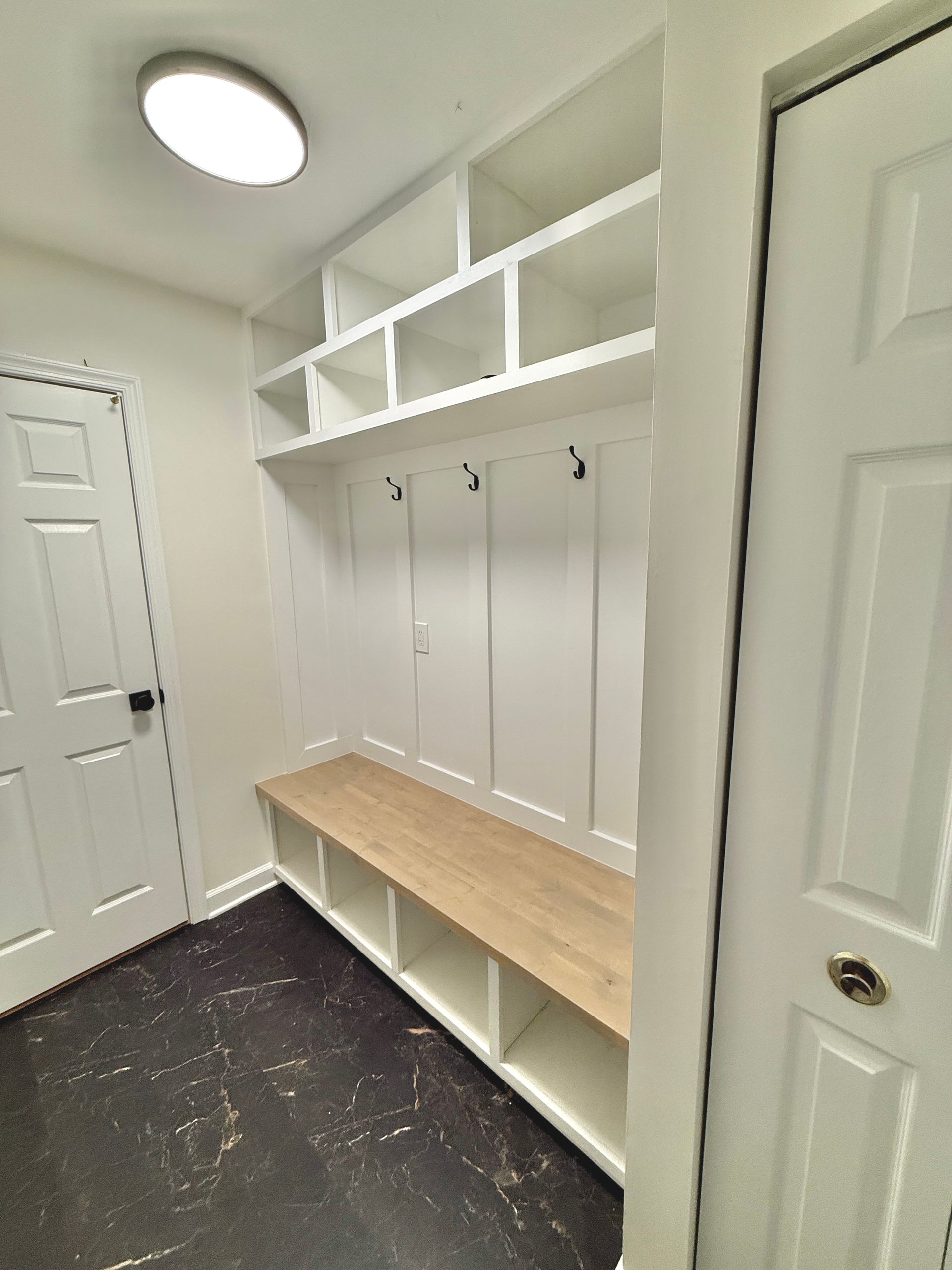 Custom mudroom bench with natural wood seating and built-in cubbies beneath custom white shelving.