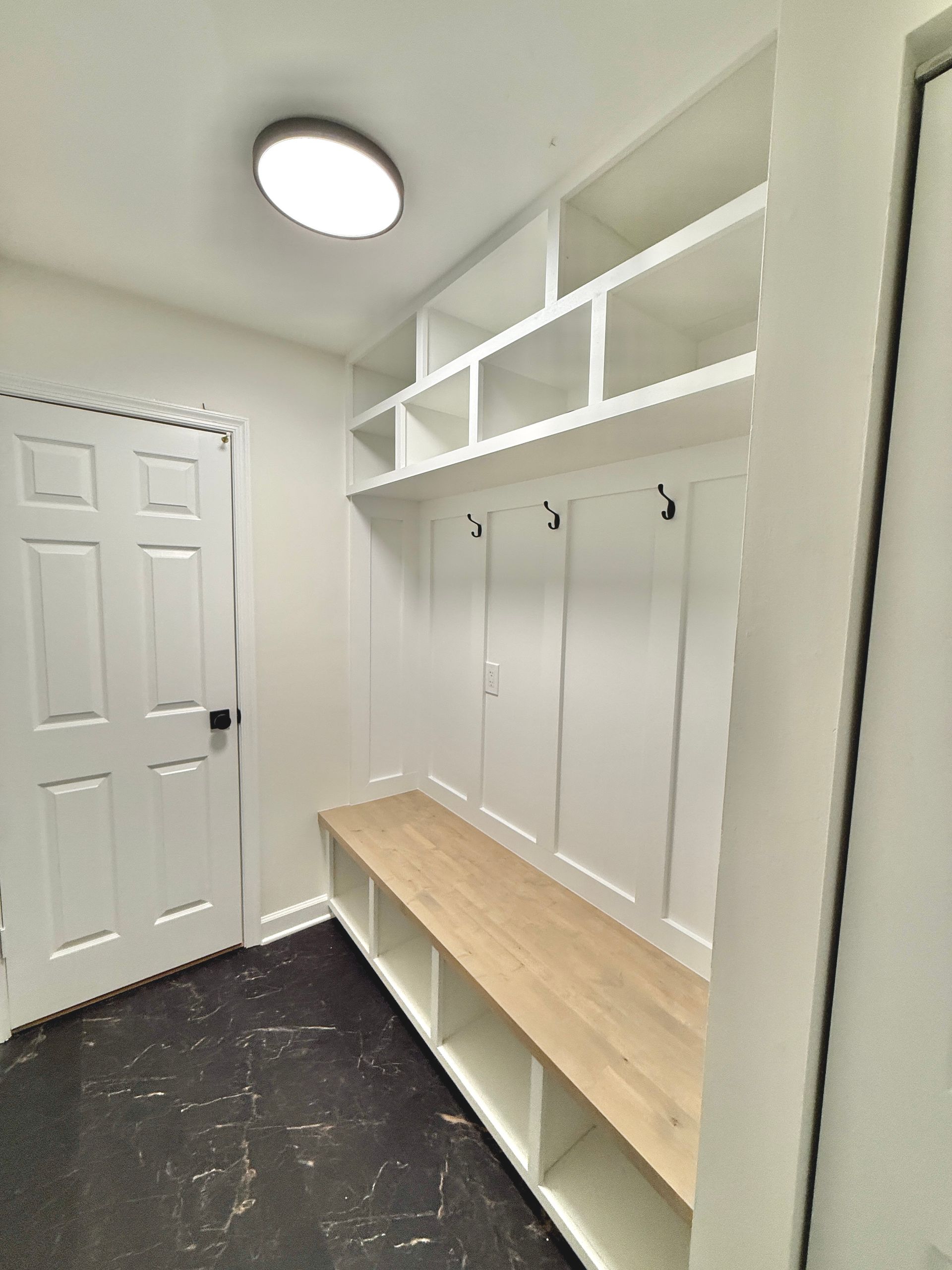 Built-in mudroom bench featuring natural wood seat, lower cubbies, and upper hooks for organization.