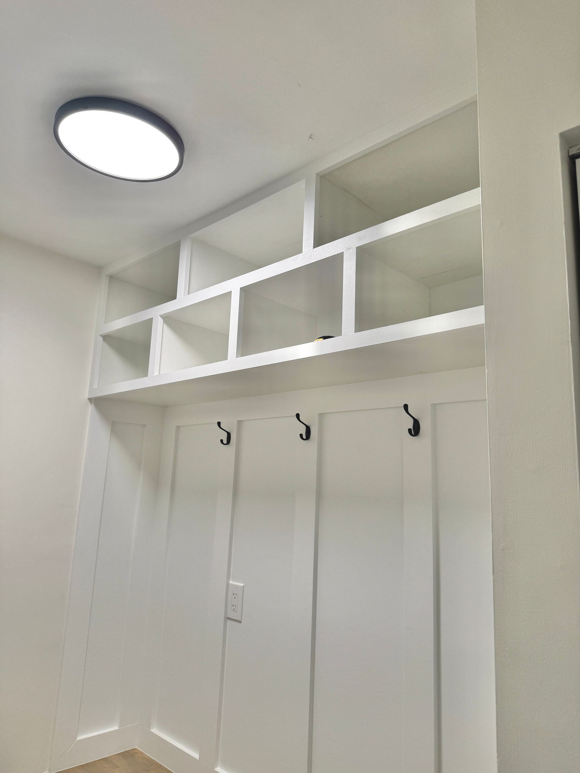 Matte black coat hooks installed on custom white board-and-batten paneling with clean lines.