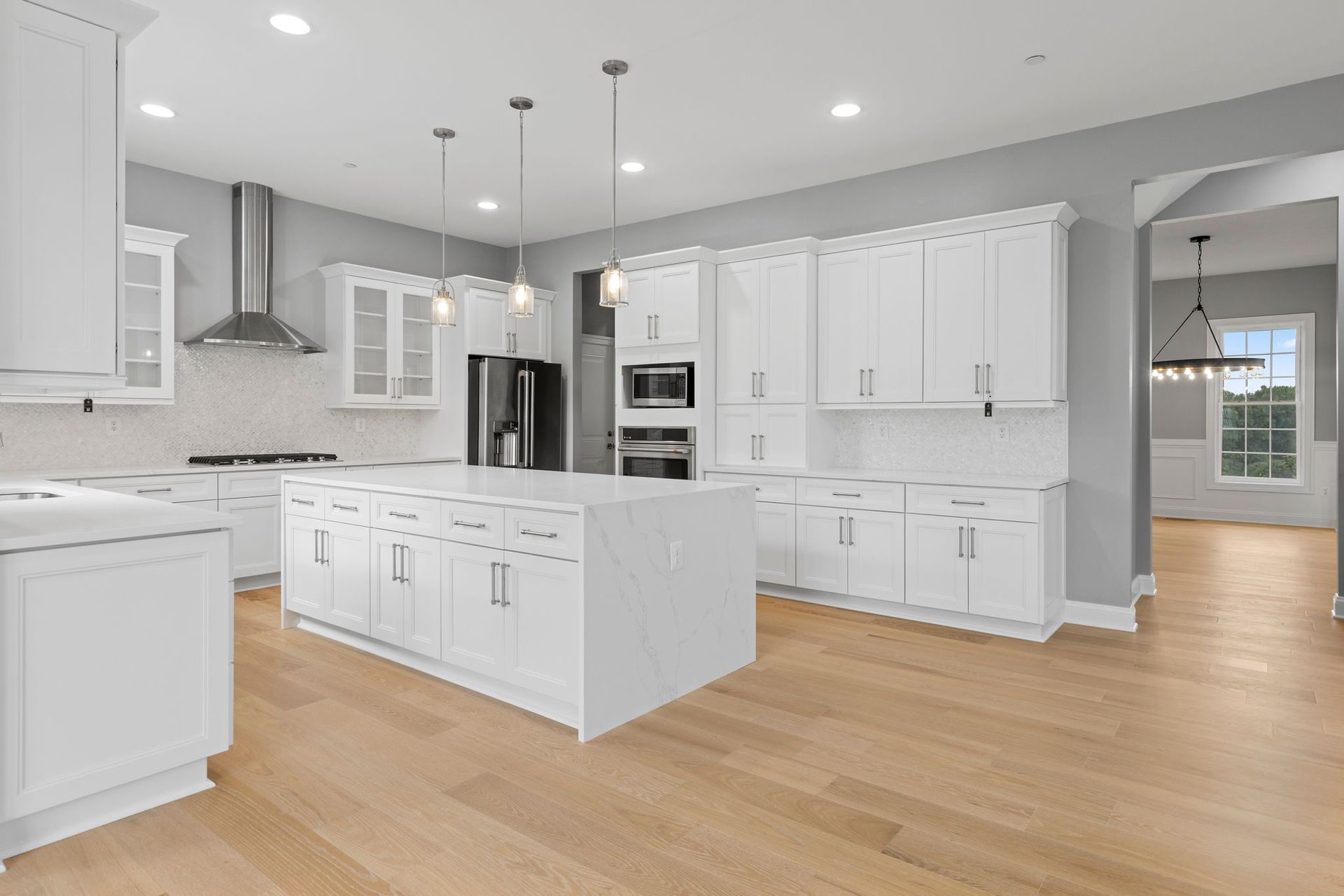 Bright open-concept kitchen renovation in Upperco, MD featuring a large waterfall quartz island and light hardwood flooring.