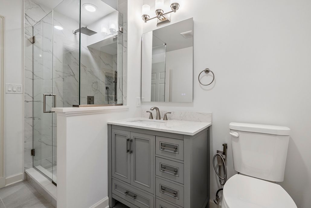 A bright, modern bathroom with a glass shower and gray vanity.