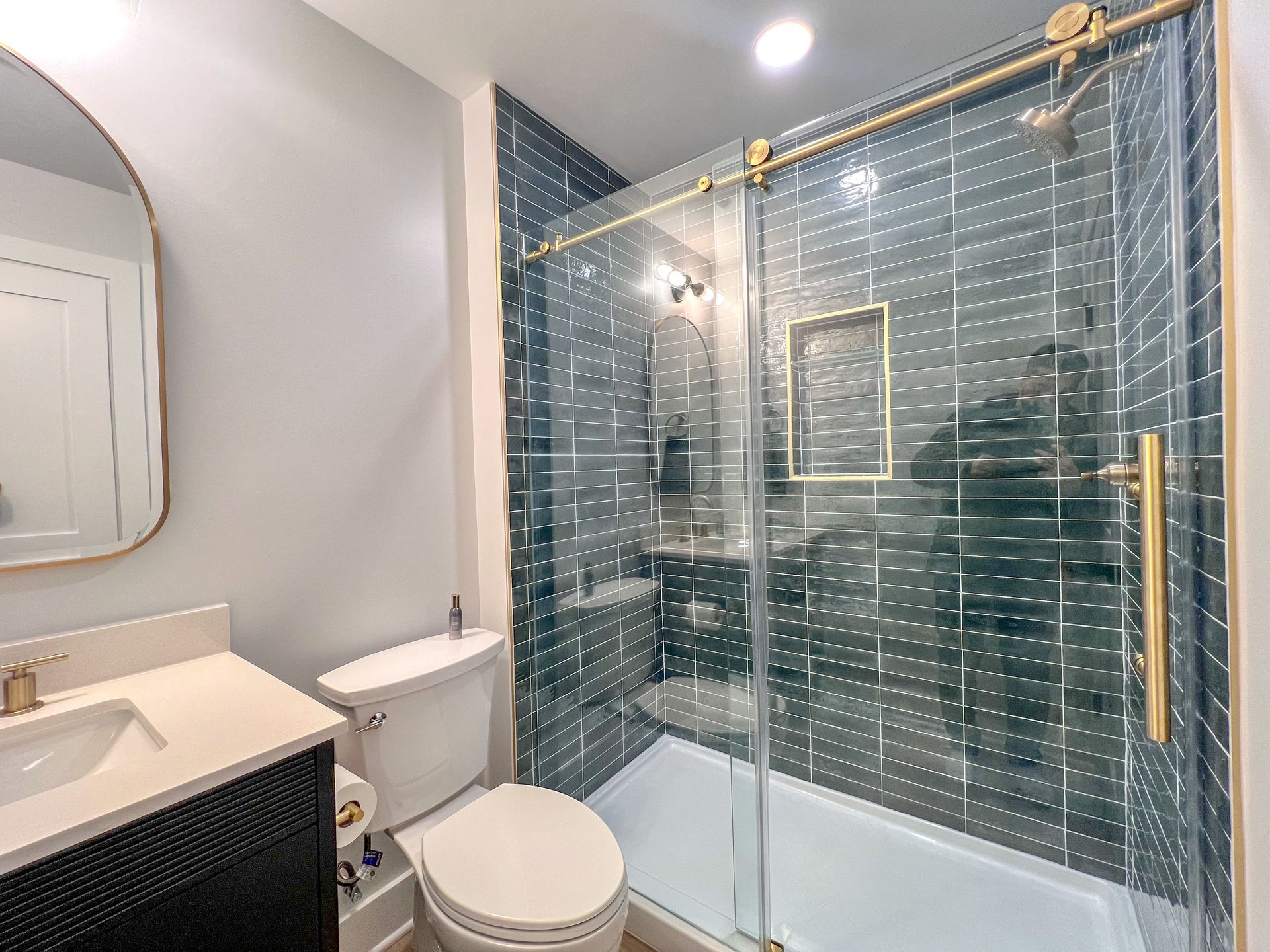 Modern bathroom with blue tiled shower and gold accents in a finished basement.