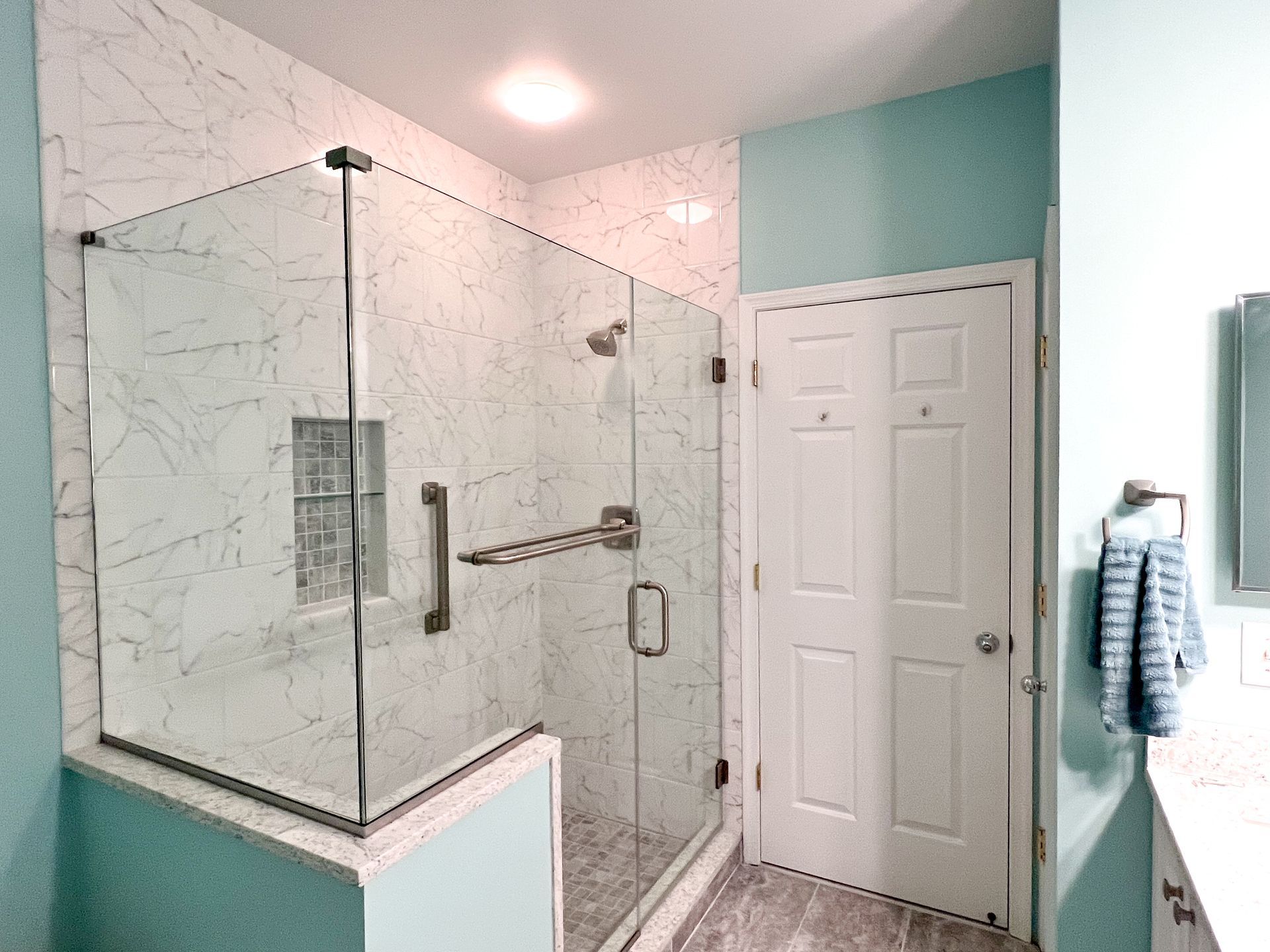 Modern walk-in shower with glass enclosure, marble-look tile, grab bars, and built-in bench in a renovated Owings Mills bathroom.