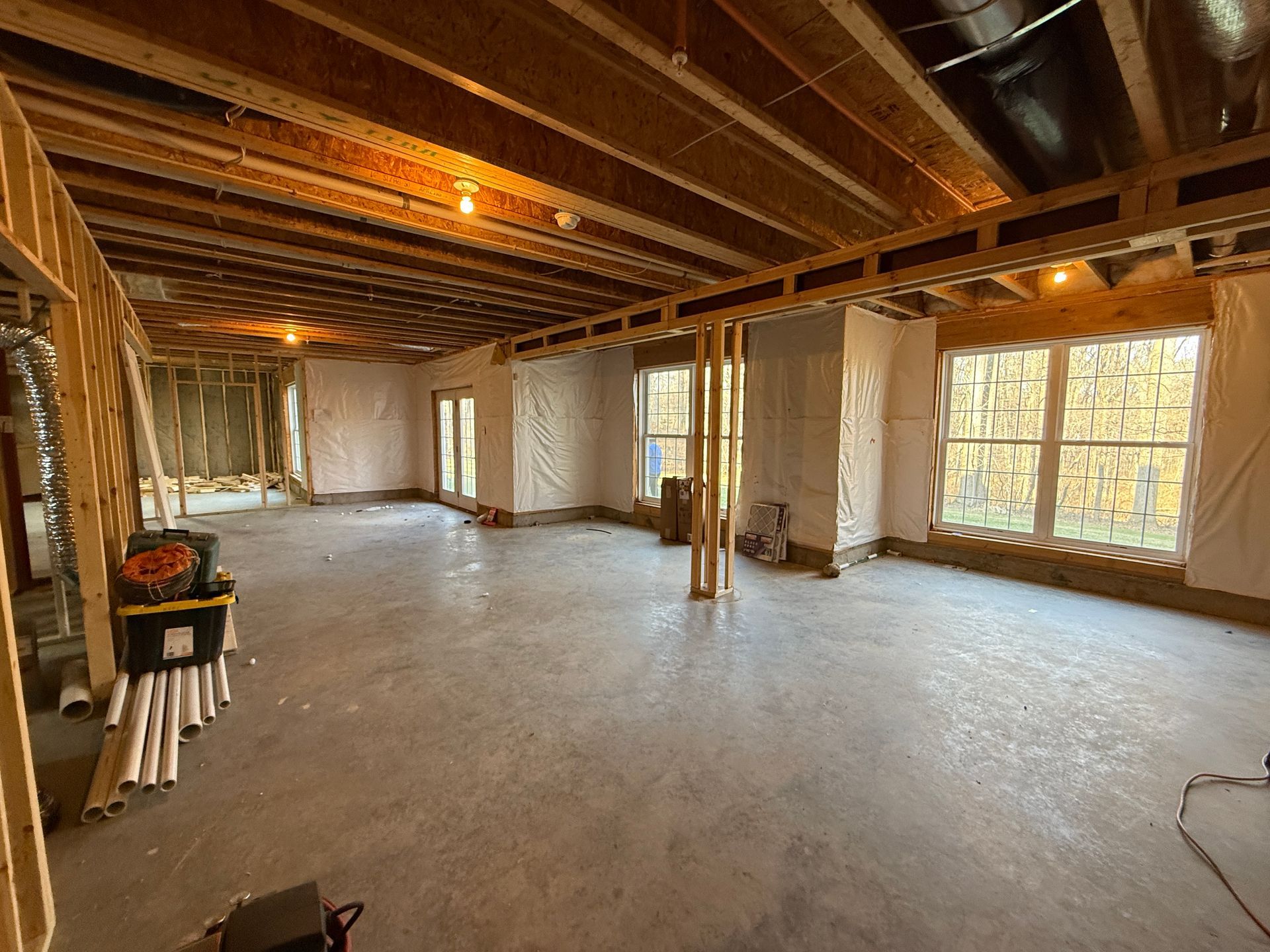 Unfinished basement studs, exposed insulation, and rough-in plumbing markings on bare concrete floor prior to bath installation.