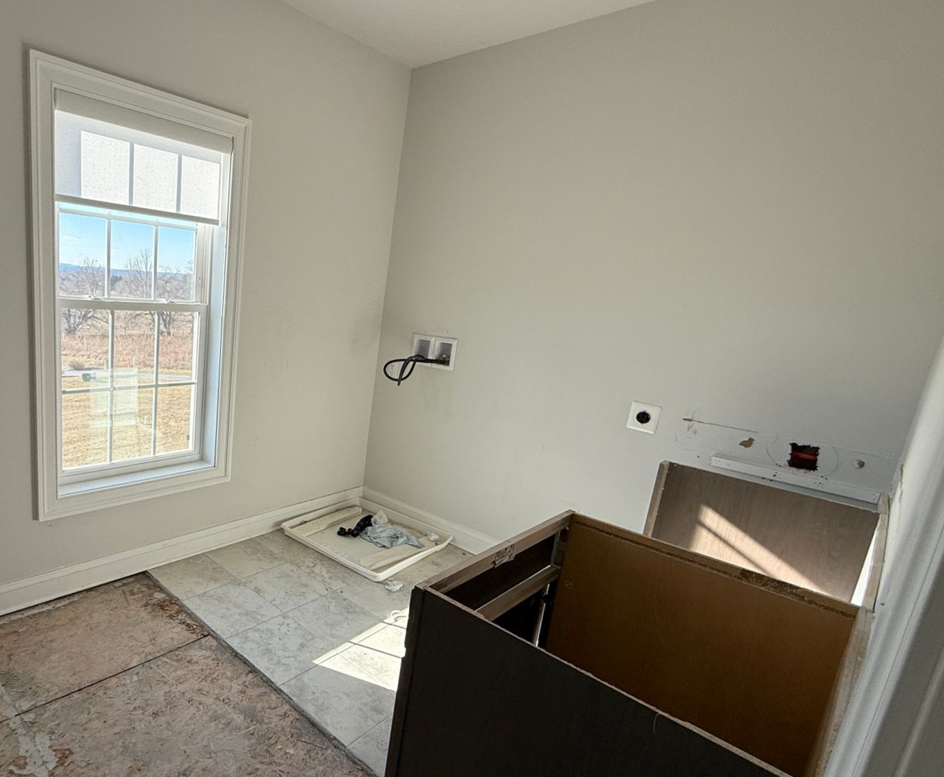 Unfinished laundry room during a home renovation, with exposed subflooring and hookups, ready for new appliances and finishes.