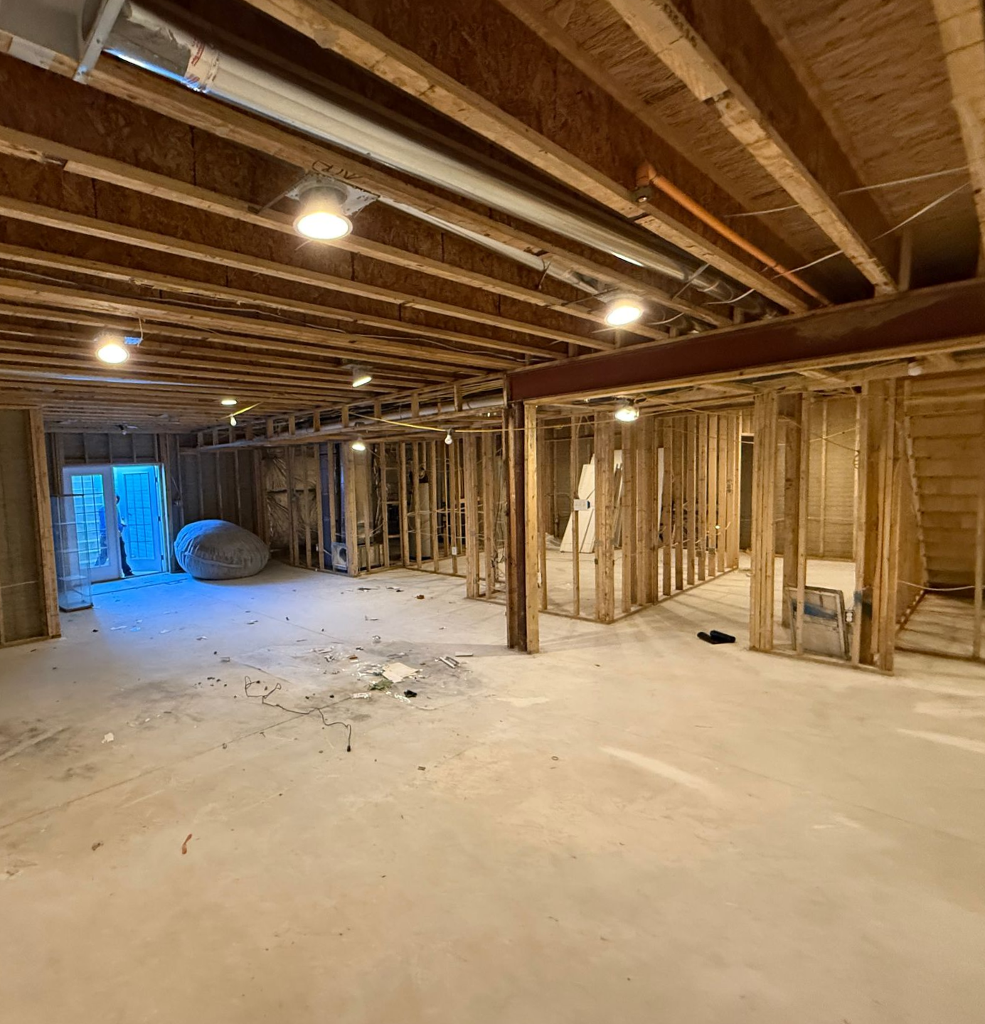 An unfinished basement during a renovation, showing exposed wood framing and a concrete floor.