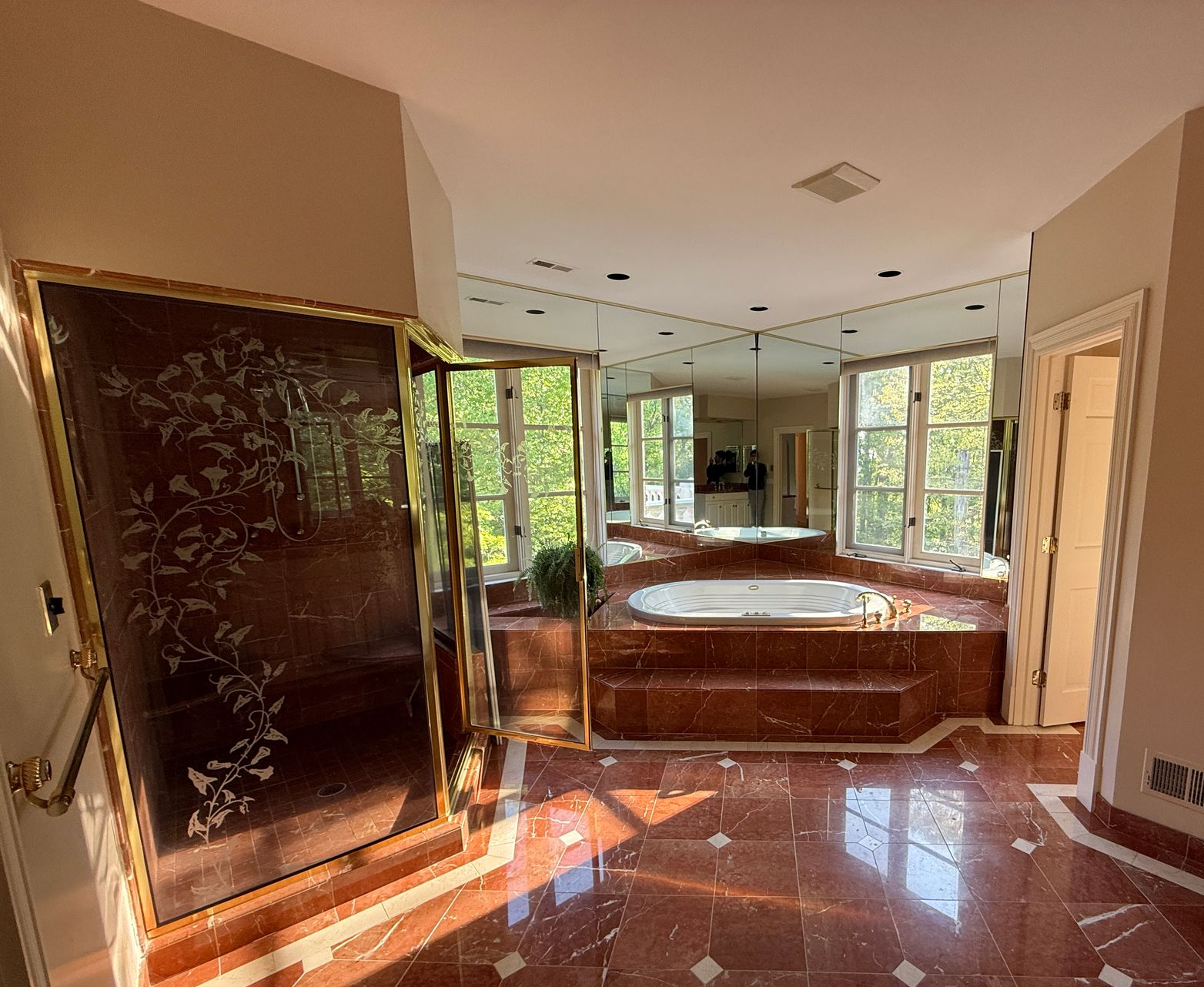 Before image of a dated Cockeysville master bathroom showing red marble-look tile, mirrored walls, a gold-framed shower, and a raised jacuzzi tub.
