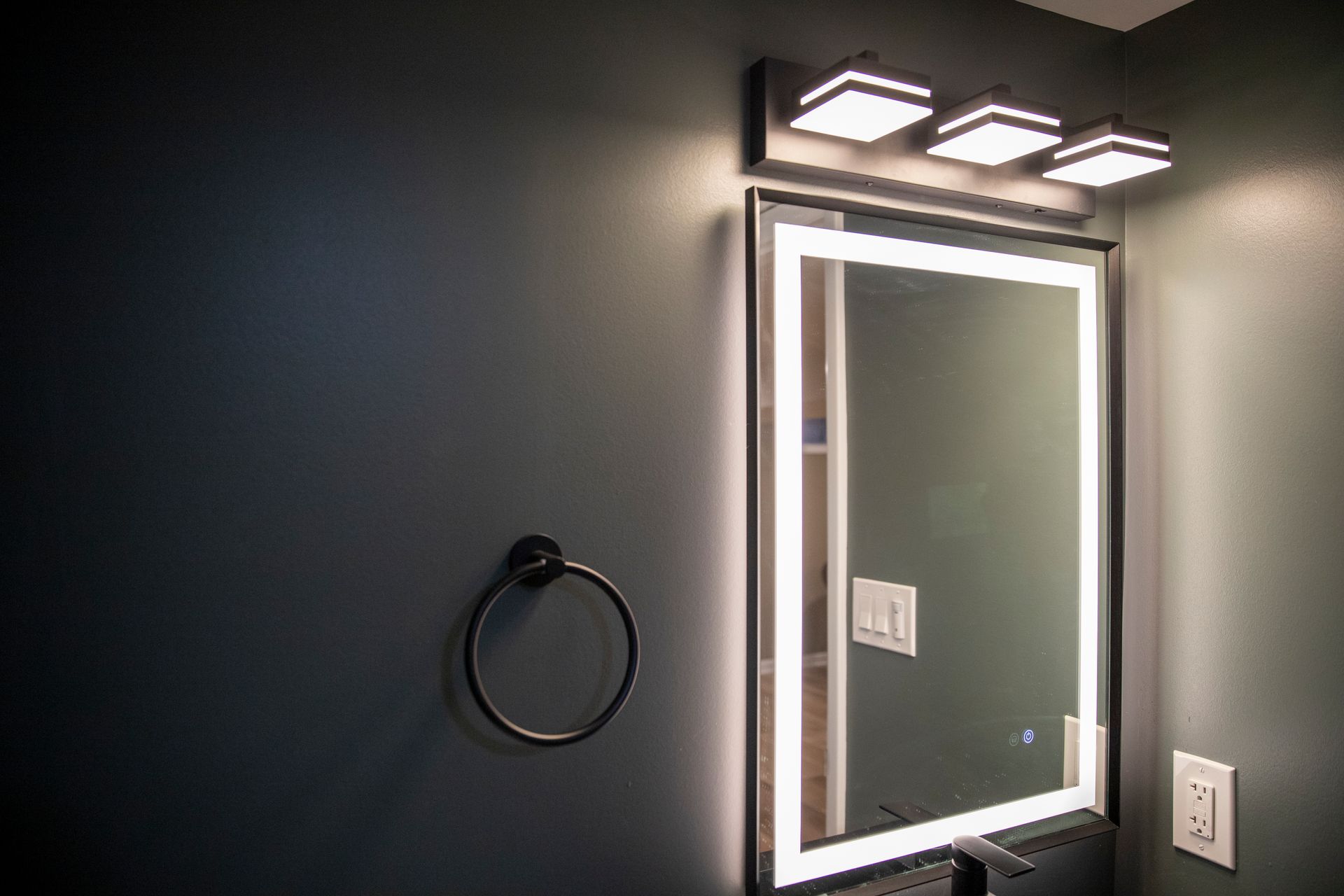 Backlit modern mirror installed over a sleek bathroom vanity.