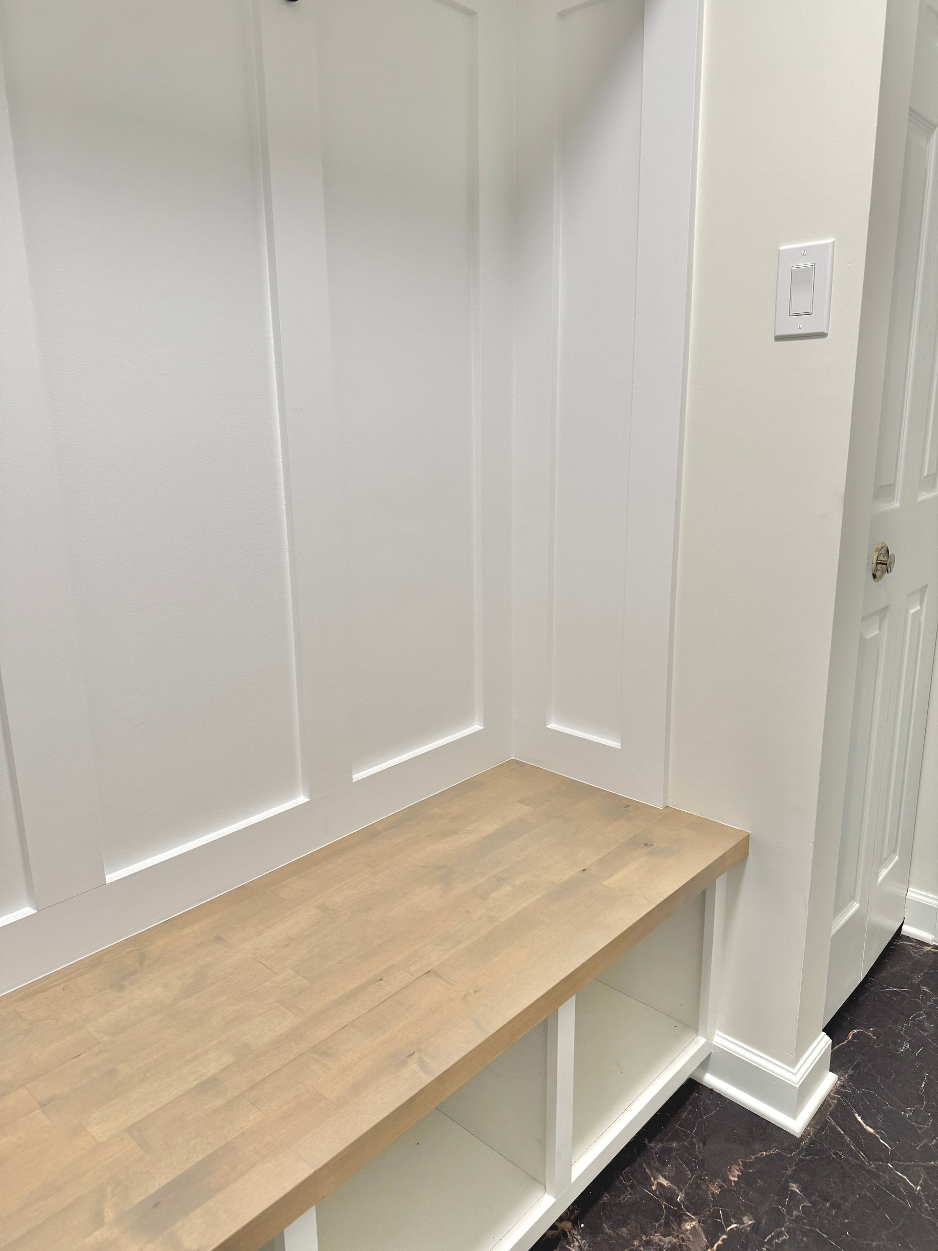 Custom-built natural wood bench seat corner with white shiplap base and door trim.