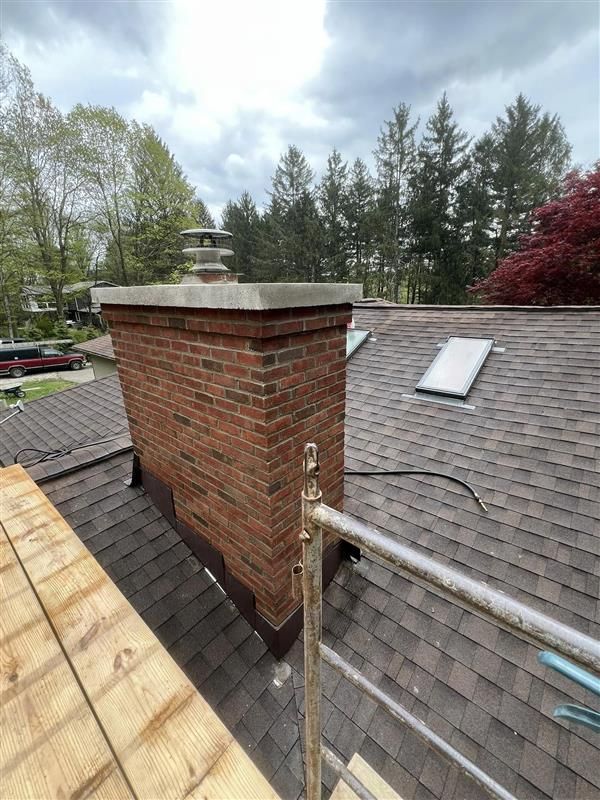 Brick chimney on a tiled roof under a blue sky, lit by the sun.