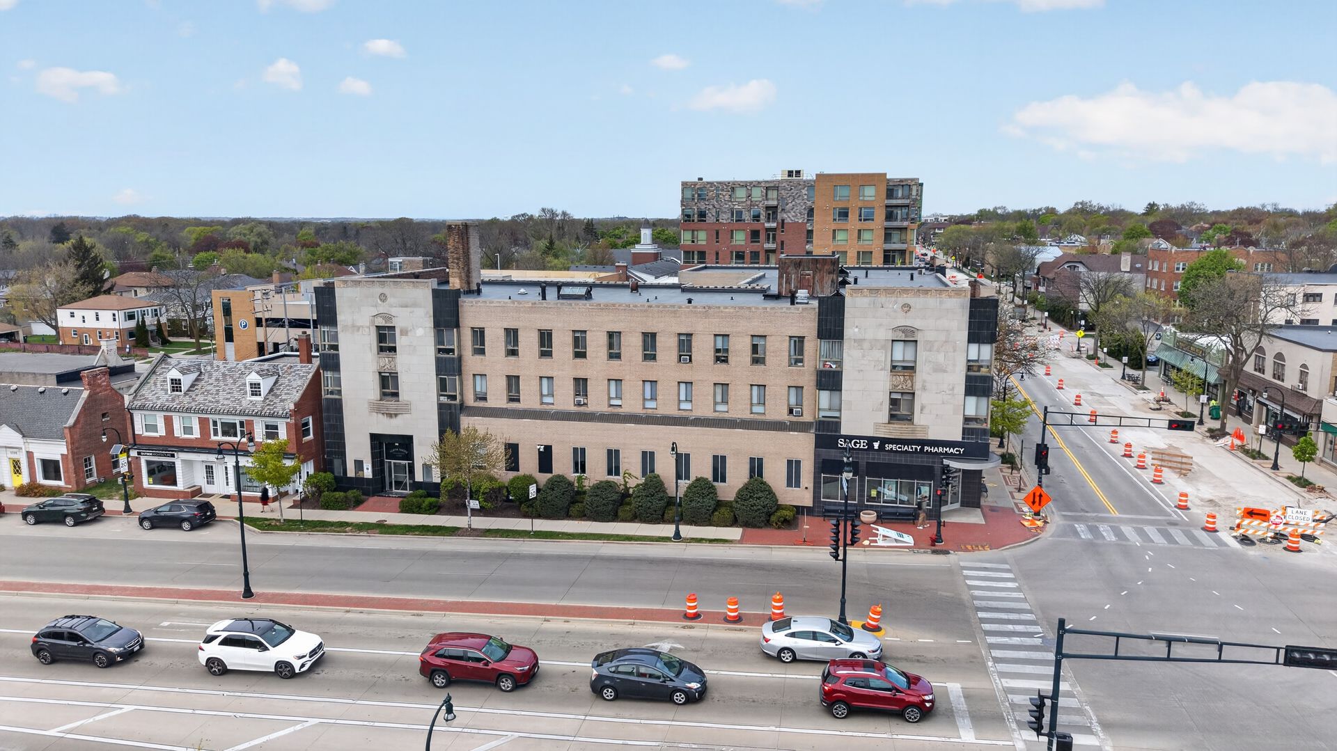 Aerial view of a beige building beside a busy street with cars and traffic cones under construction.