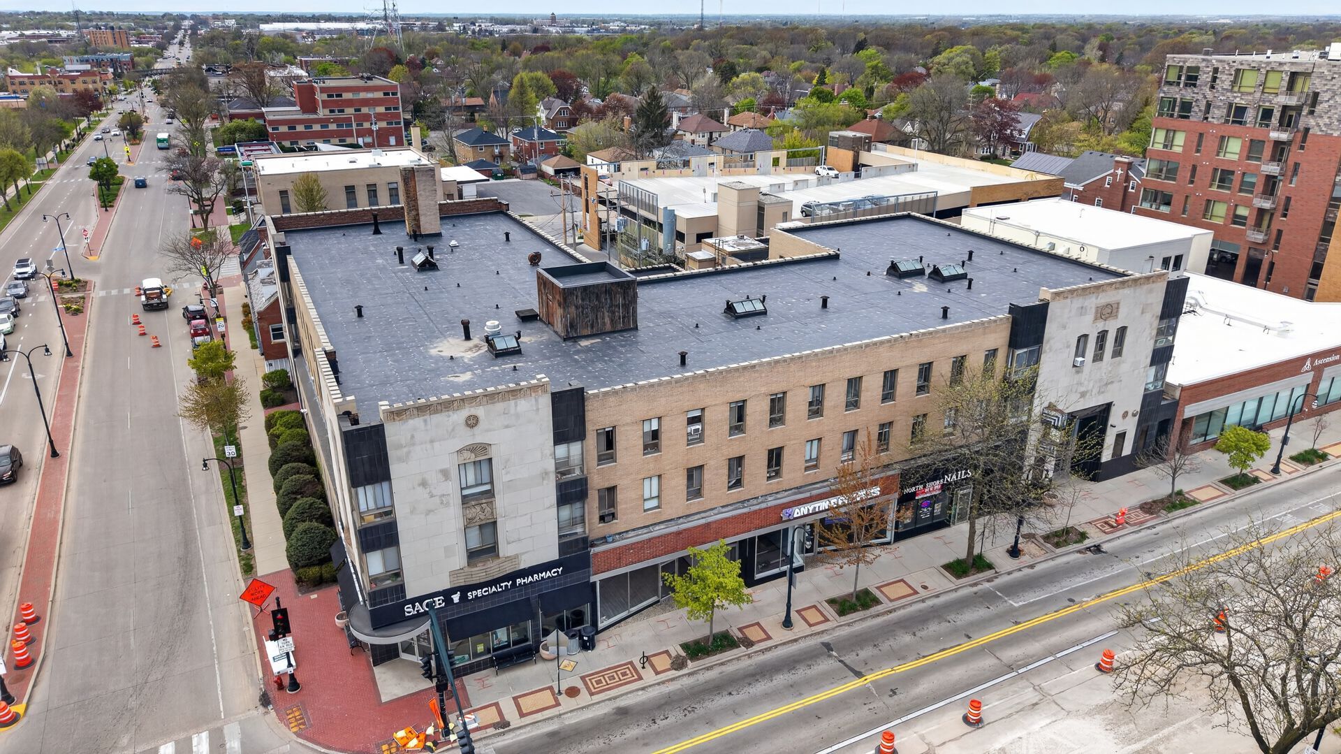 Aerial view of a large beige building on a city street with cars, sidewalks, and surrounding neighborhood.
