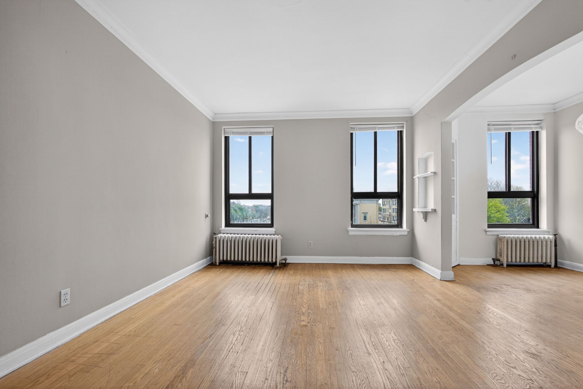 Empty modern room with hardwood floors, gray walls, tall windows, and white radiators
