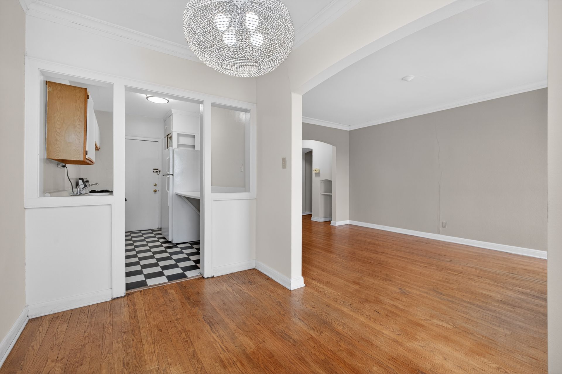 Bright empty living room with hardwood floors, white walls, and a small tiled bathroom doorway.