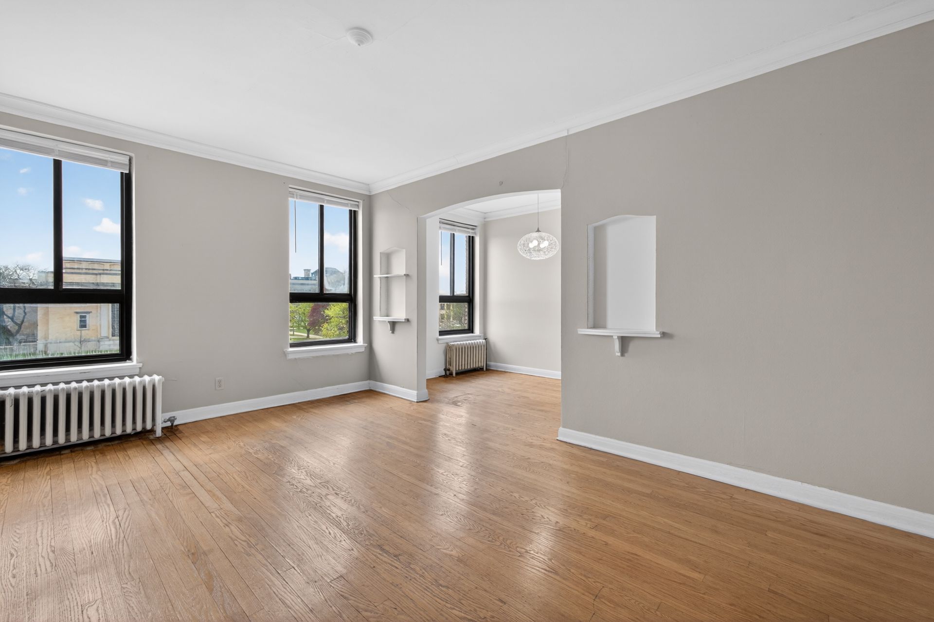 Empty modern room with wood floors, gray walls, large windows, and a wall mirror.