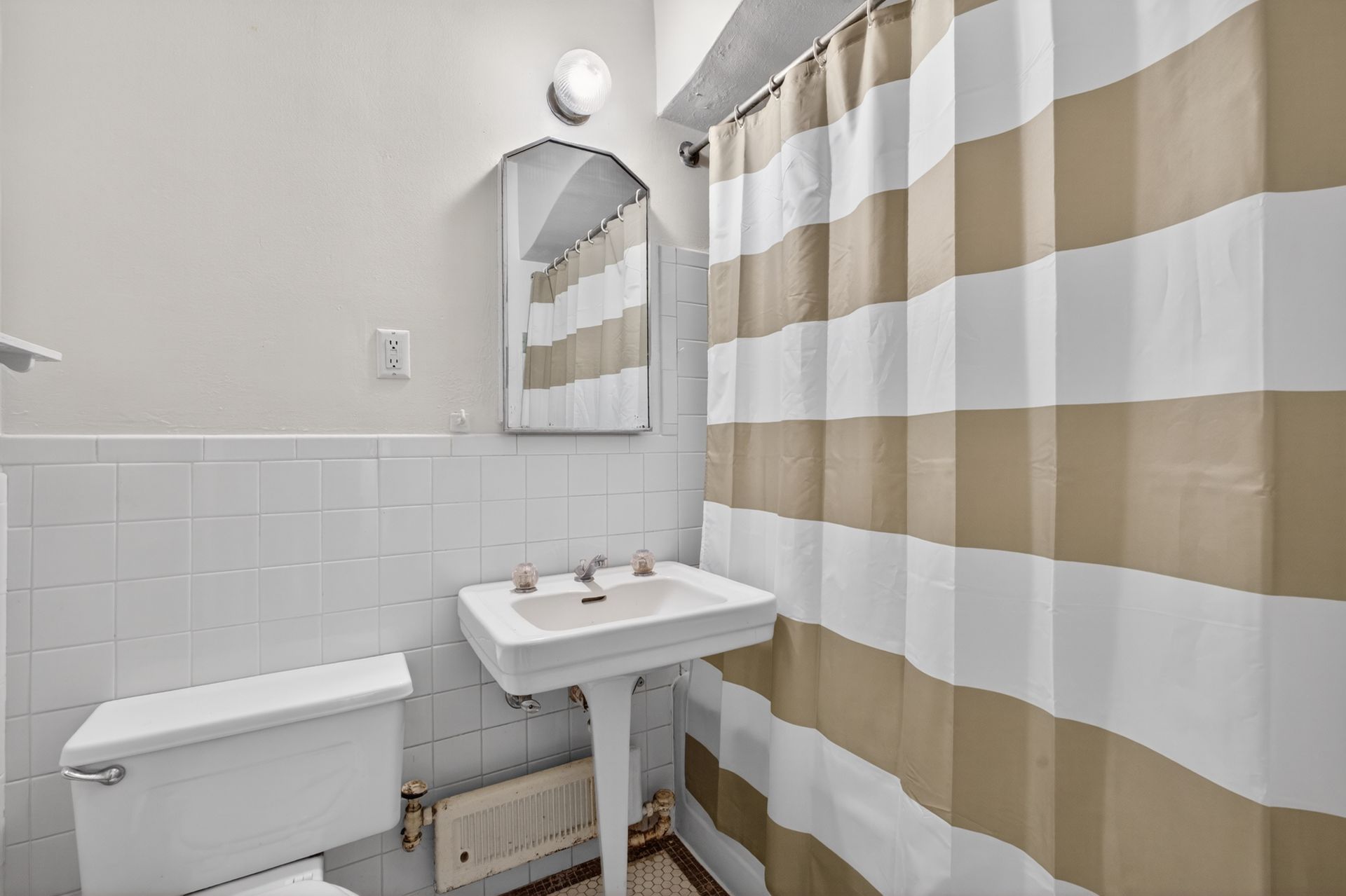Small bathroom with toilet, sink, mirror, and beige-and-white striped shower curtain.