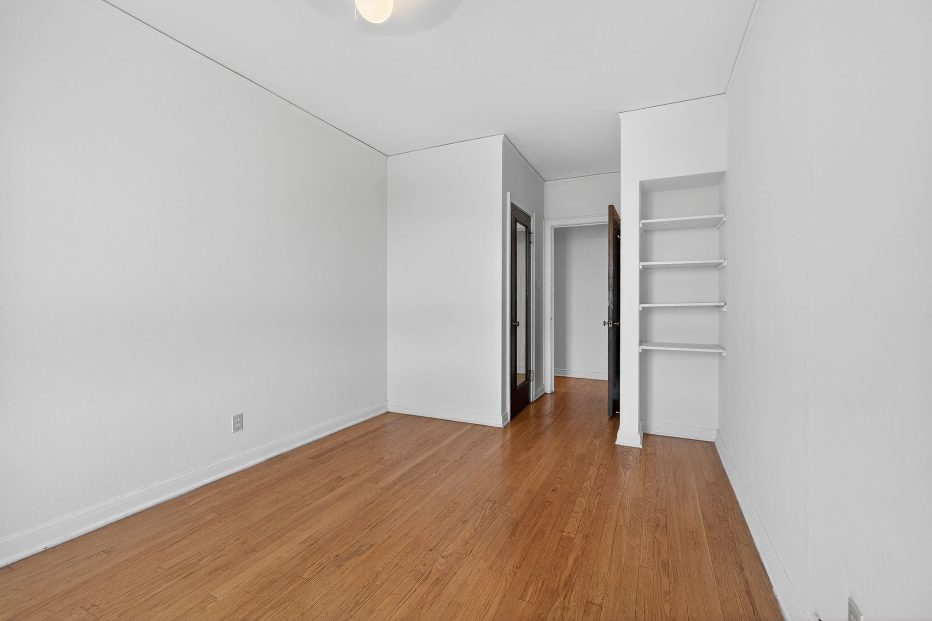 Empty white room with wood floor, built-in shelves, and a doorway in back.