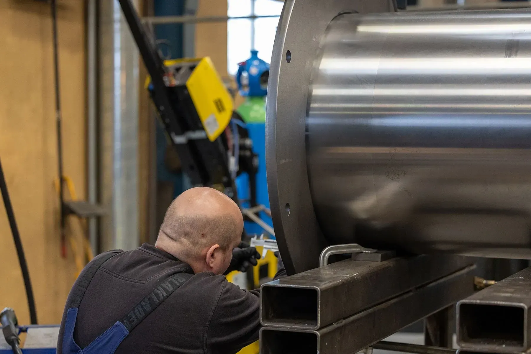 Arbejder inspicerer en stor metalcylinder i et industrielt værksted