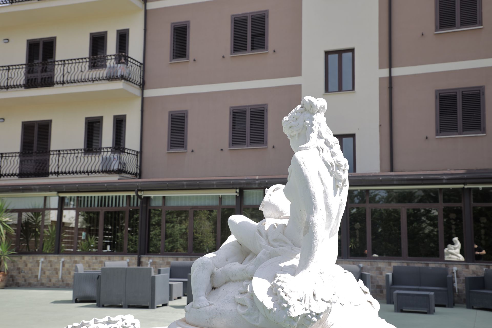 Una scultura in marmo bianco raffigurante una figura si erge di fronte a un moderno edificio alberghiero con balconi e finestre incorniciate di scuro.