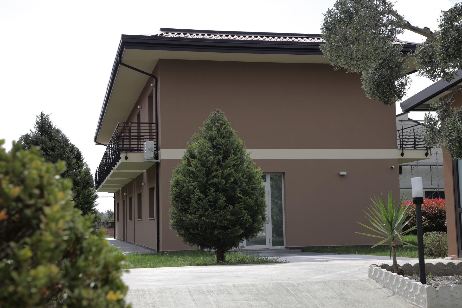 Un edificio a due piani, di colore beige, con un balcone, che si intravede tra la vegetazione circostante e il paesaggio esterno.