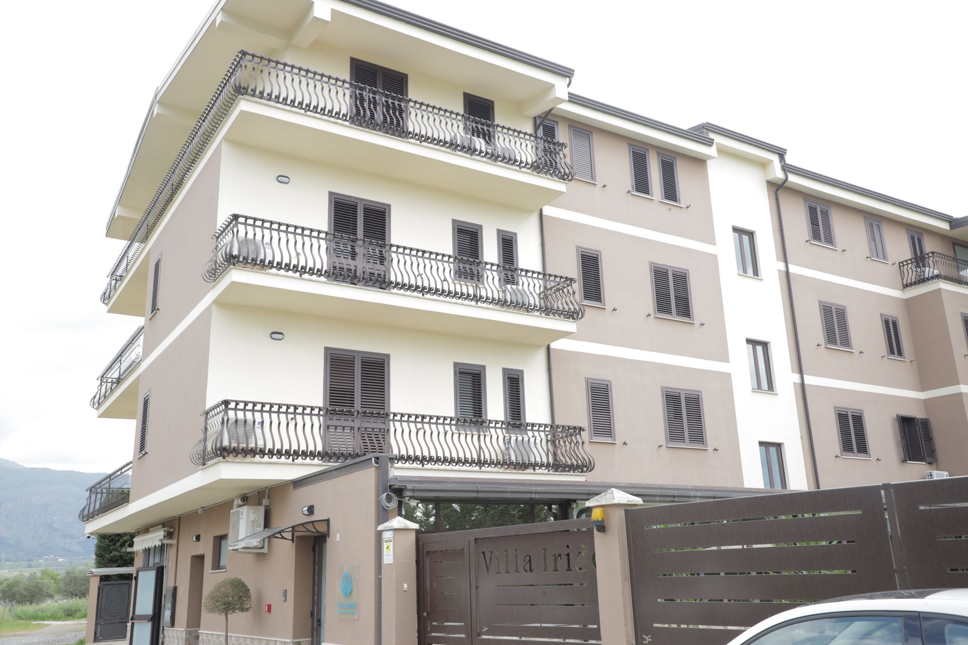Un moderno edificio residenziale di quattro piani con pareti chiare, finestre con infissi scuri e balconi in ferro.