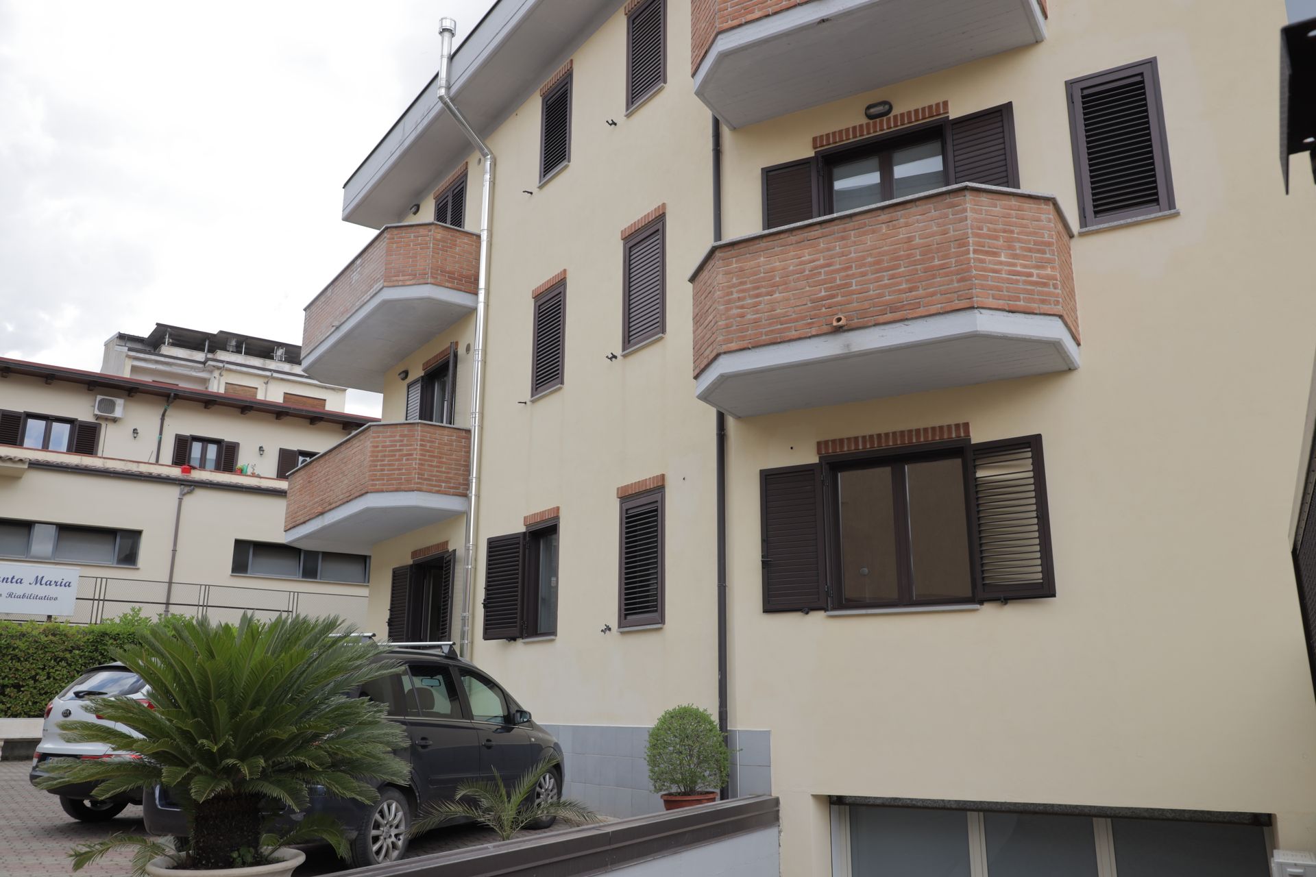 Una vista dal basso di un condominio a più piani con pareti beige, balconi con dettagli in mattoni e un'auto parcheggiata sottostante.