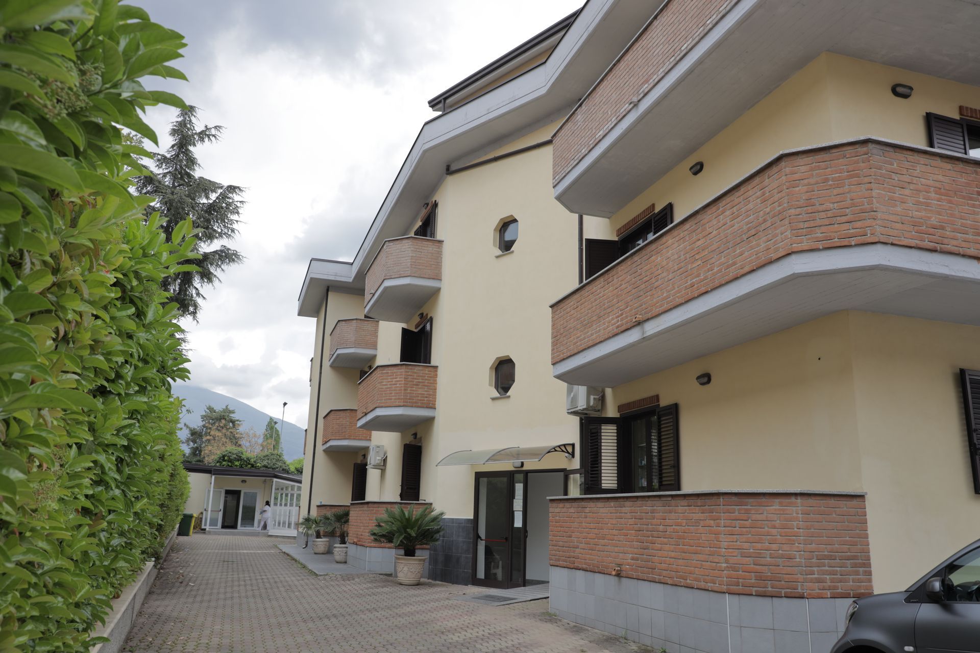 Un condominio di tre piani con pareti beige e balconi rifiniti in mattoni, situato accanto a un vialetto pavimentato.