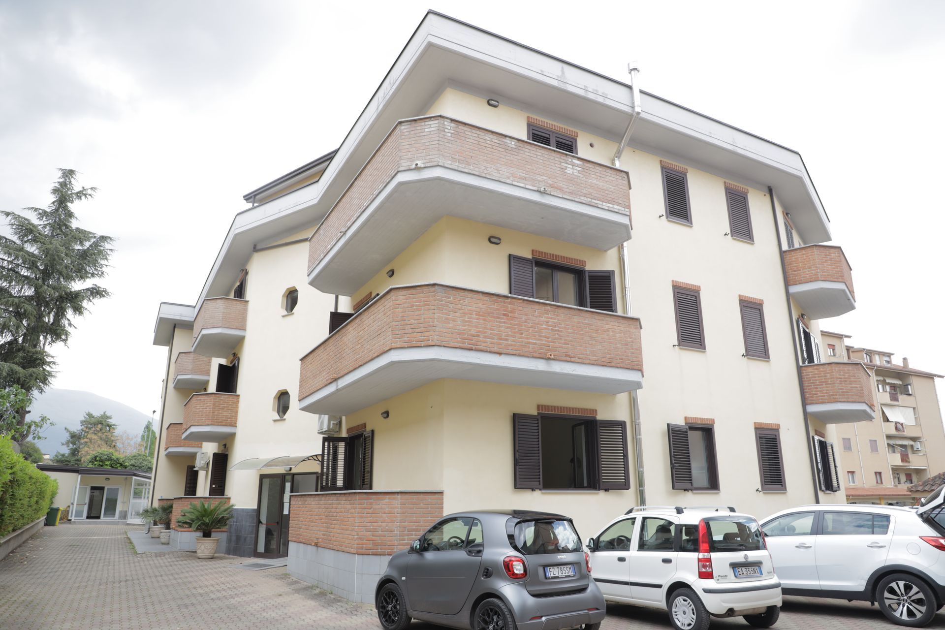 Un condominio a più piani con pareti beige e balconi con dettagli in mattoni, con auto parcheggiate in primo piano.